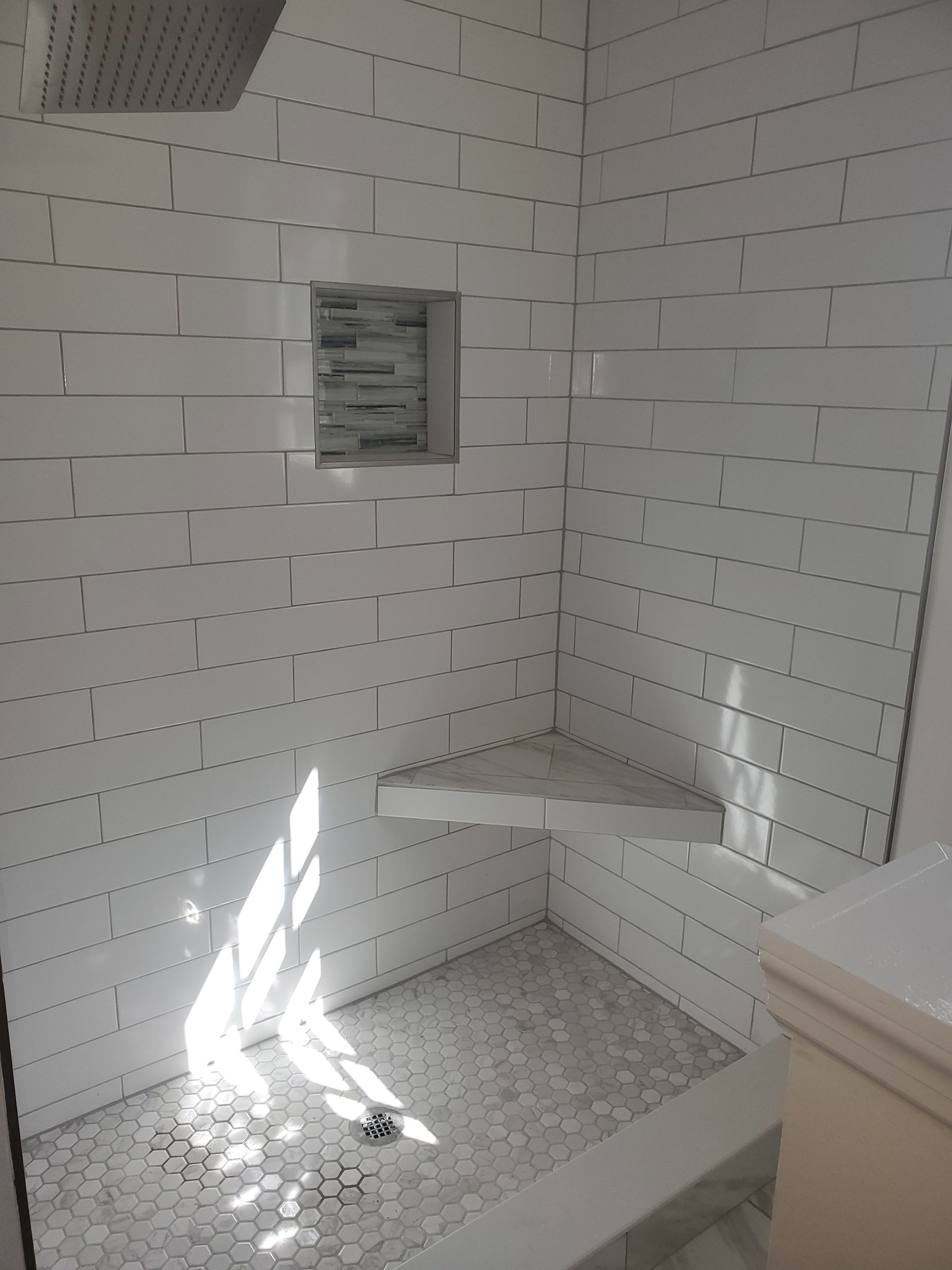 White tiled shower with a corner seat, niche, and hexagon floor tiling.