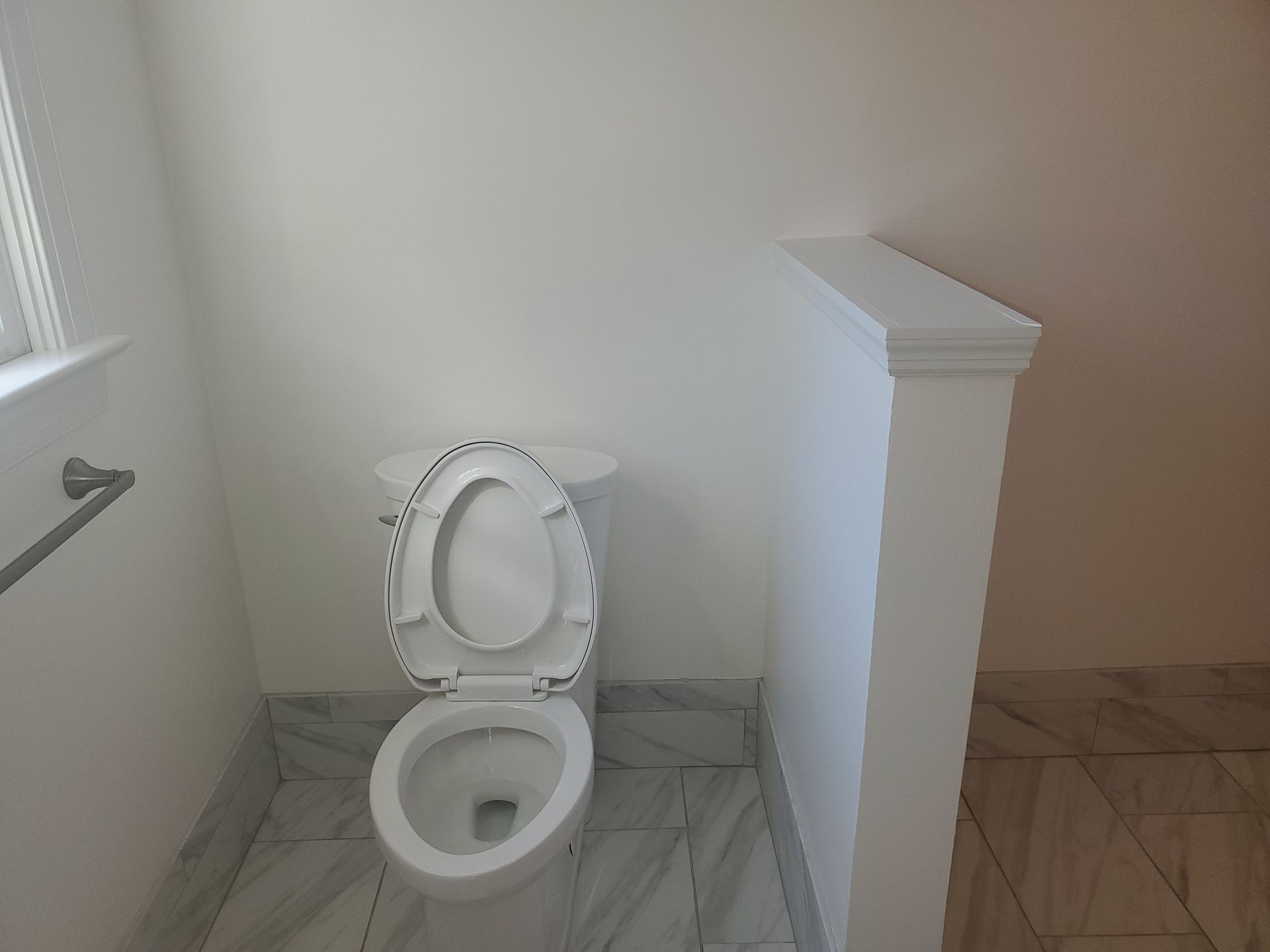 Toilet in a small bathroom with marble floor, white walls, and a partial partition.