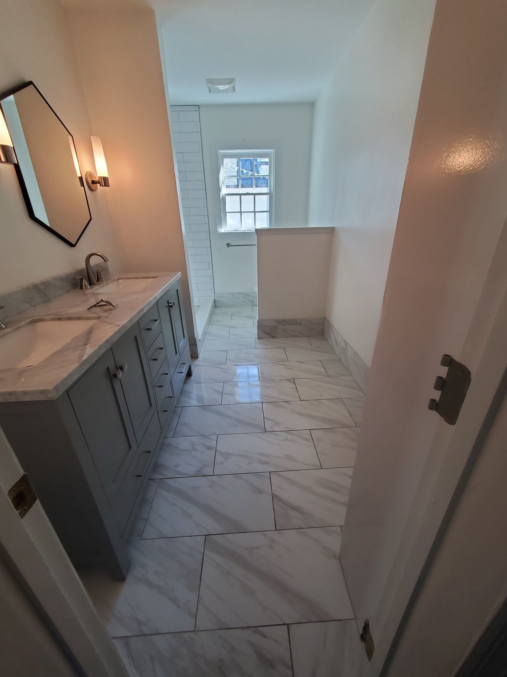 Bathroom with marble tile floor, gray vanity, and decorative mirror.