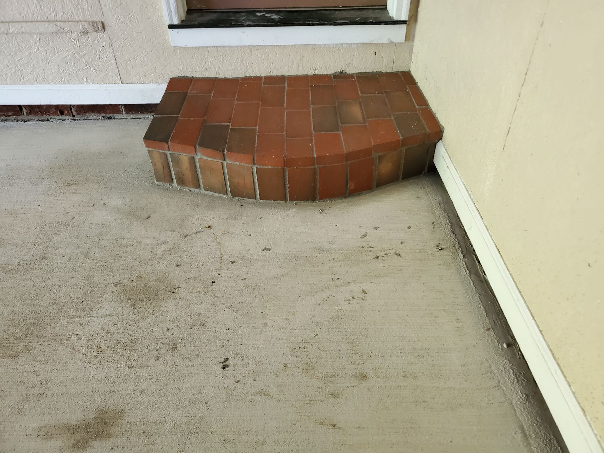 Concrete porch with brick step leading to a doorway, adjacent to a beige wall.