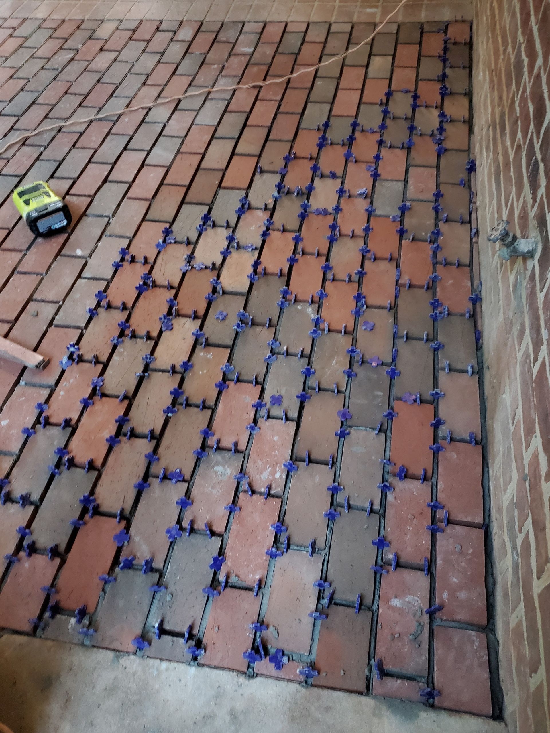 Brick pavers laid in a herringbone pattern with blue leveling clips, next to a brick wall.