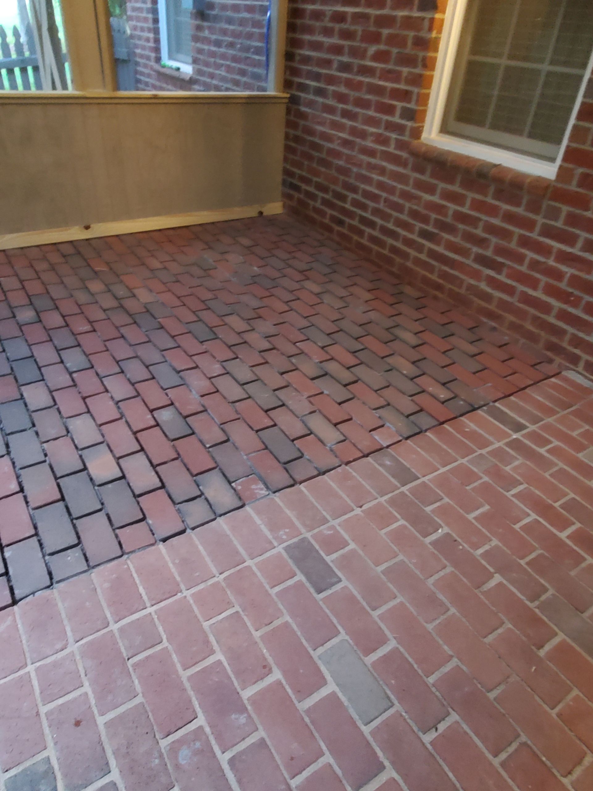 Red brick patio with two distinct color variations, adjacent to a brick wall and a window.