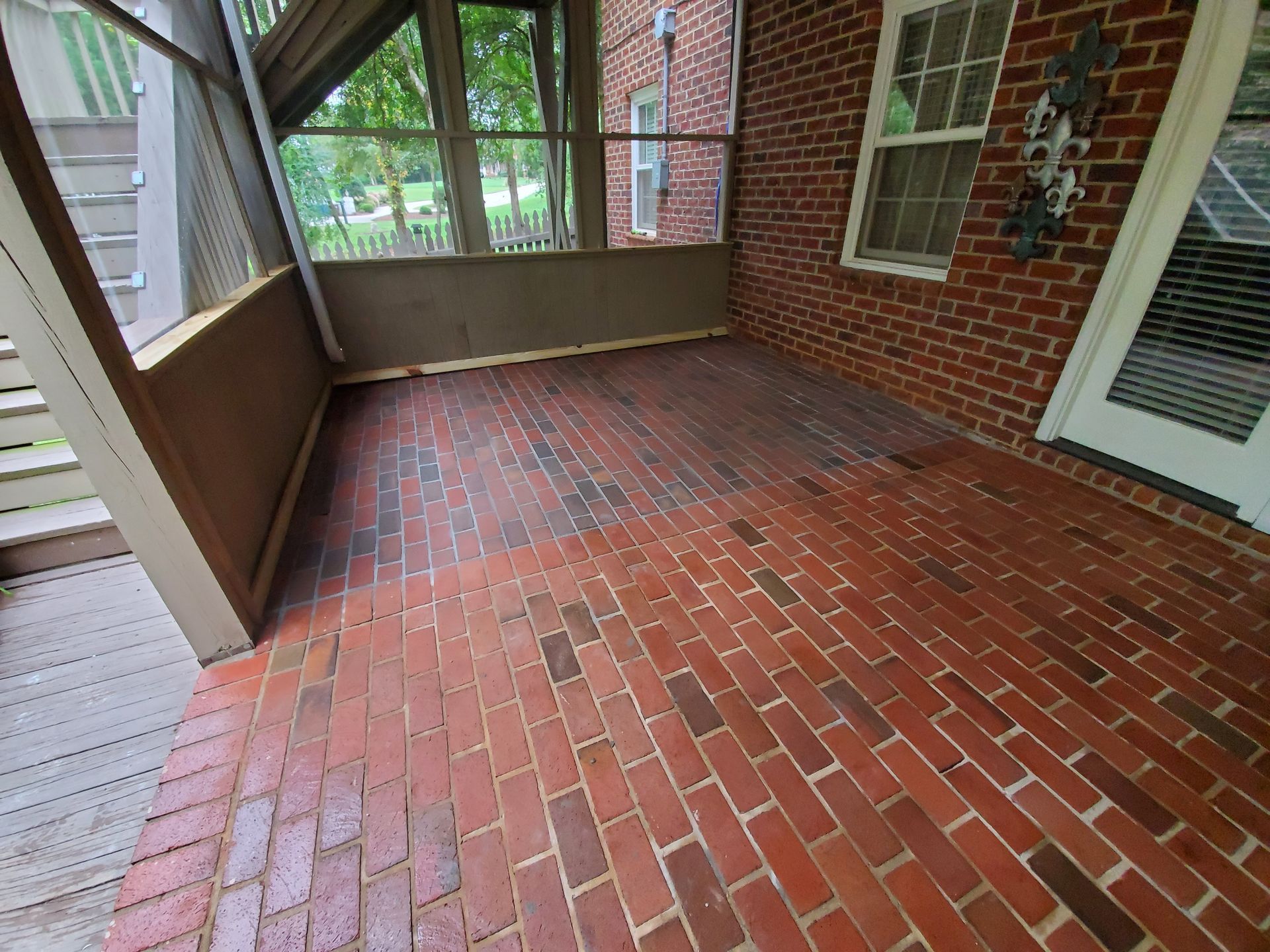 Brick-paved porch with screened walls, brick walls, and a white door; a wooden staircase is visible on the left.