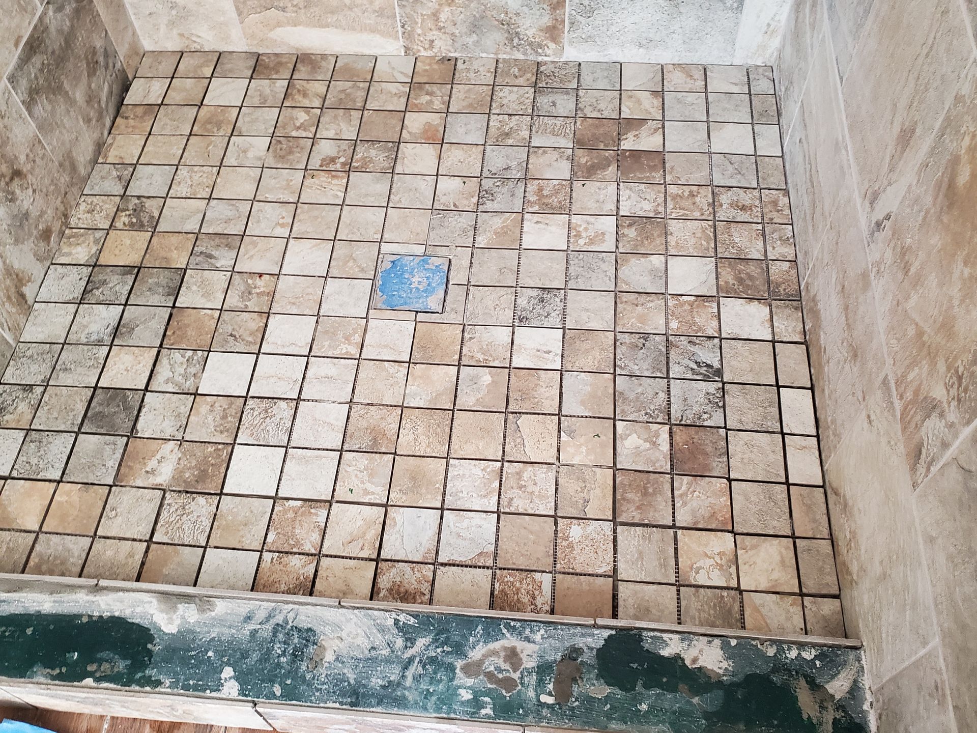 Shower floor tiled with small, square, beige and brown stones, with blue drain cover.