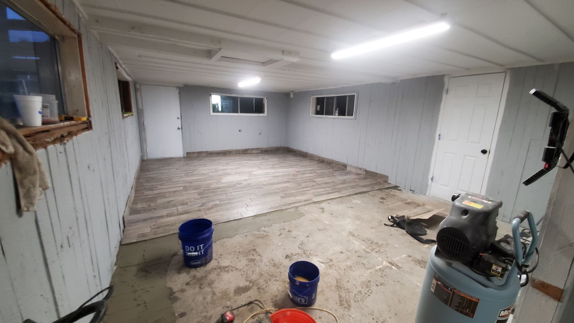 An unfinished basement with gray walls, a concrete floor, two doors, and an air compressor.