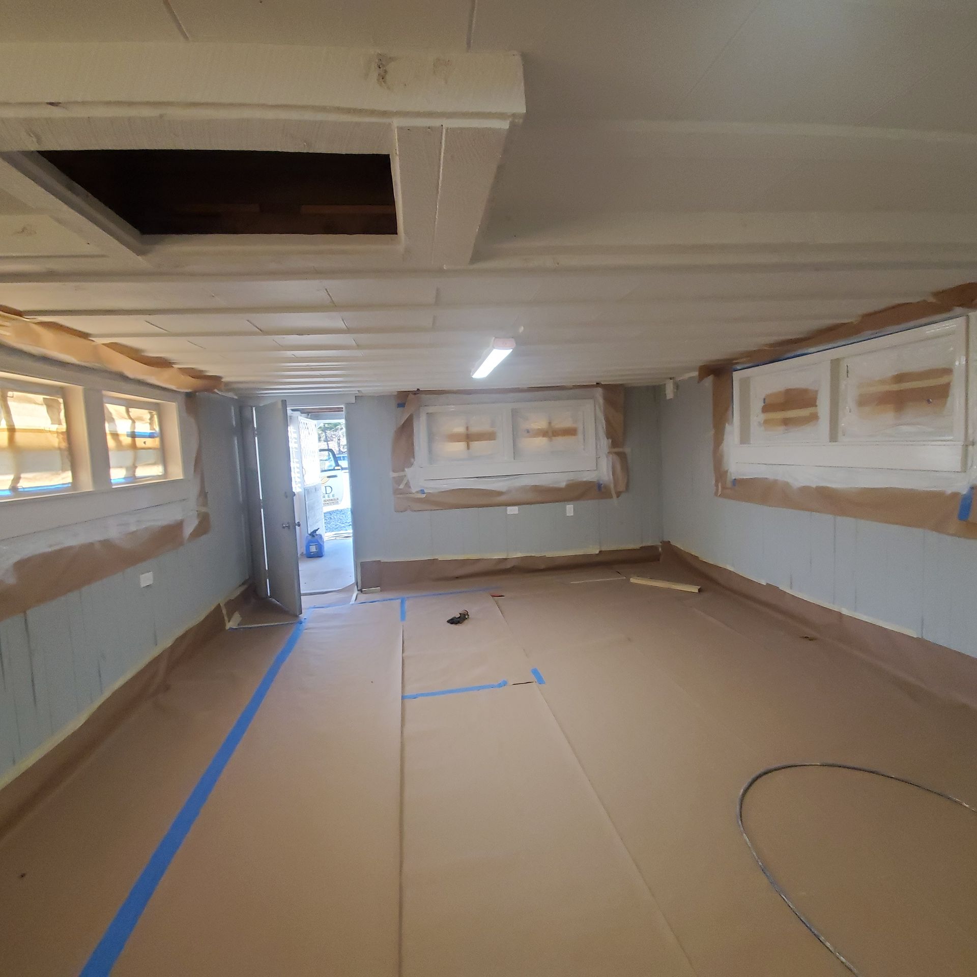 Basement interior during renovation, with taped windows, cardboard floor covering, and open door.