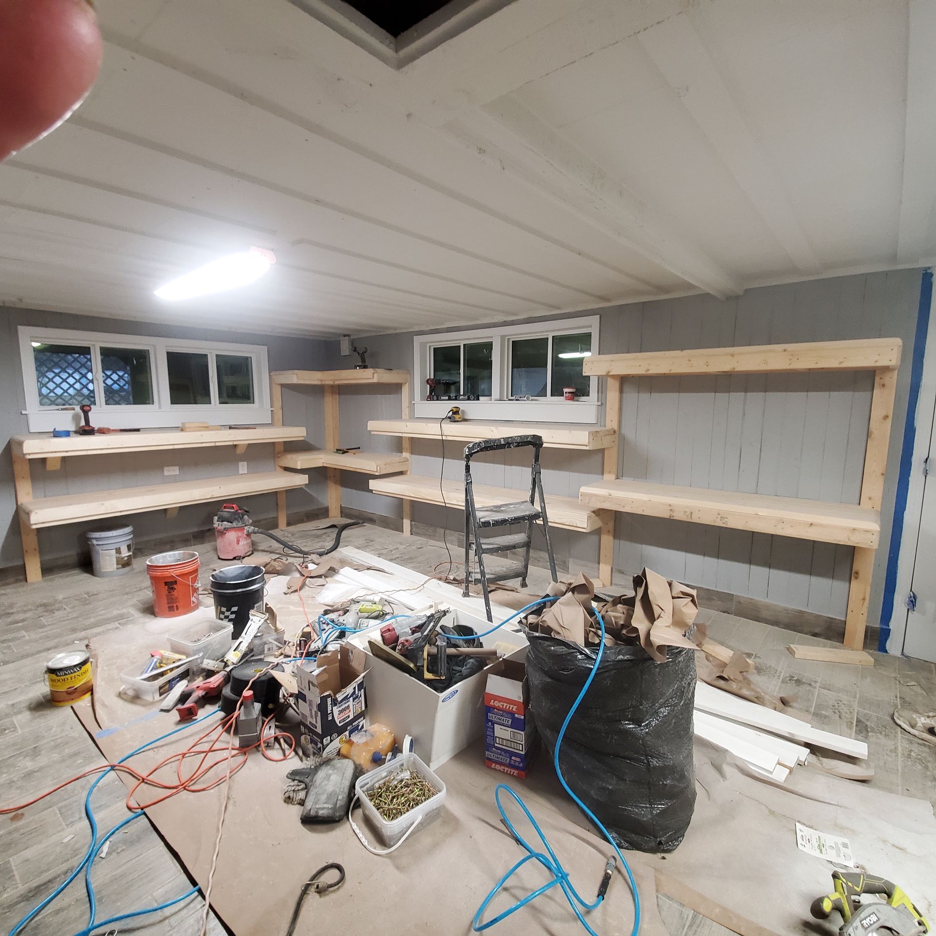 Workshop interior with unfinished wooden shelves and tools scattered on the floor.