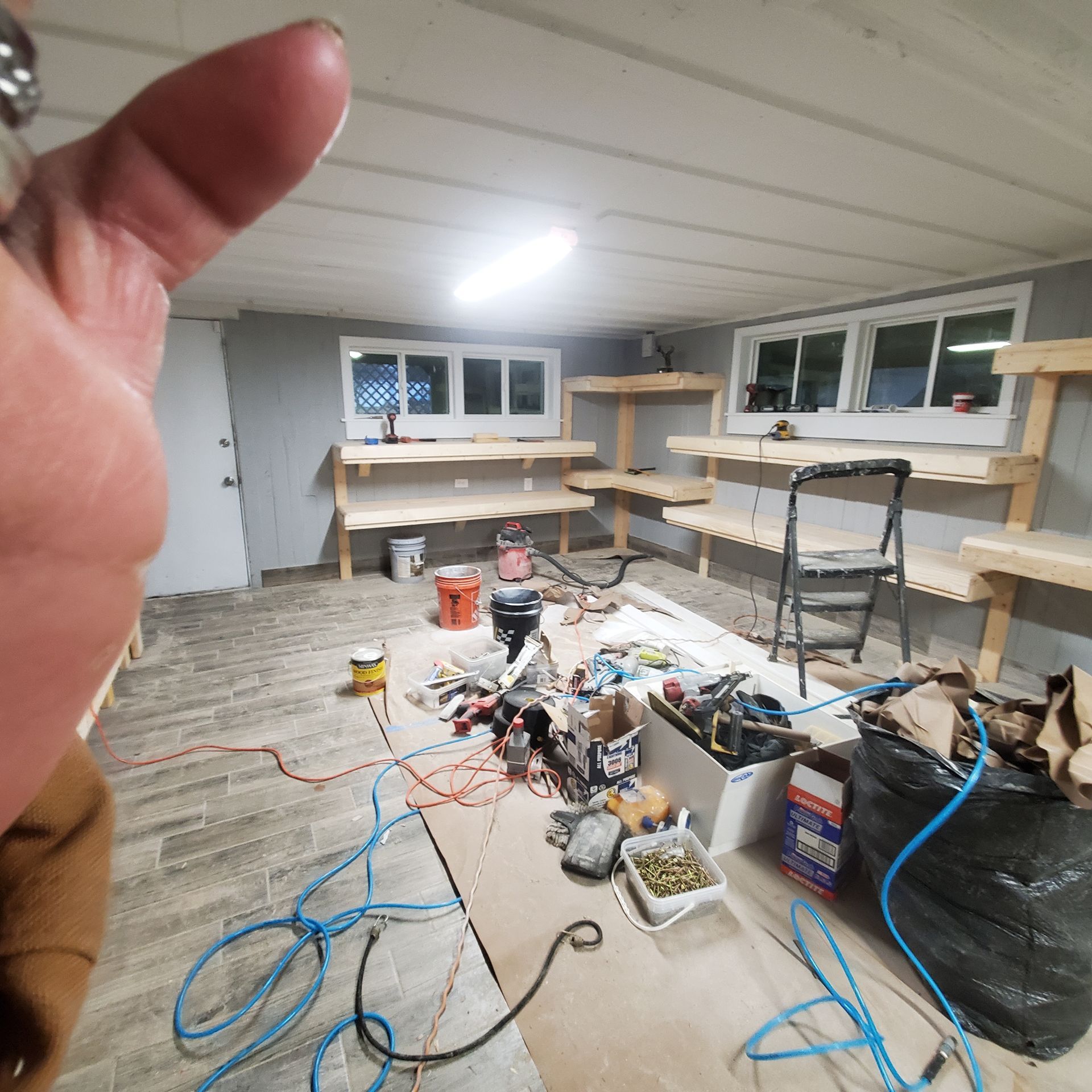 Interior room under construction, with shelving, tools, and a person's hand in view.