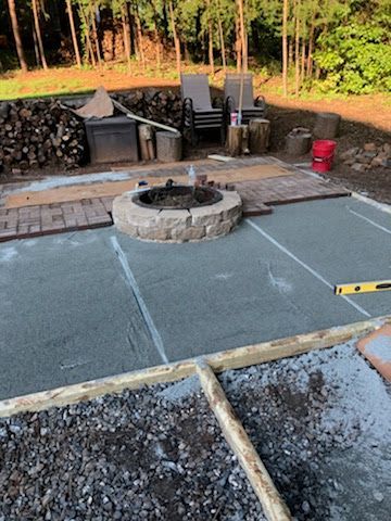 Concrete patio being constructed with a stone fire pit, wood, and landscaping.
