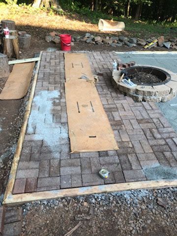 Brick patio under construction, with fire pit and wood plank pathway.