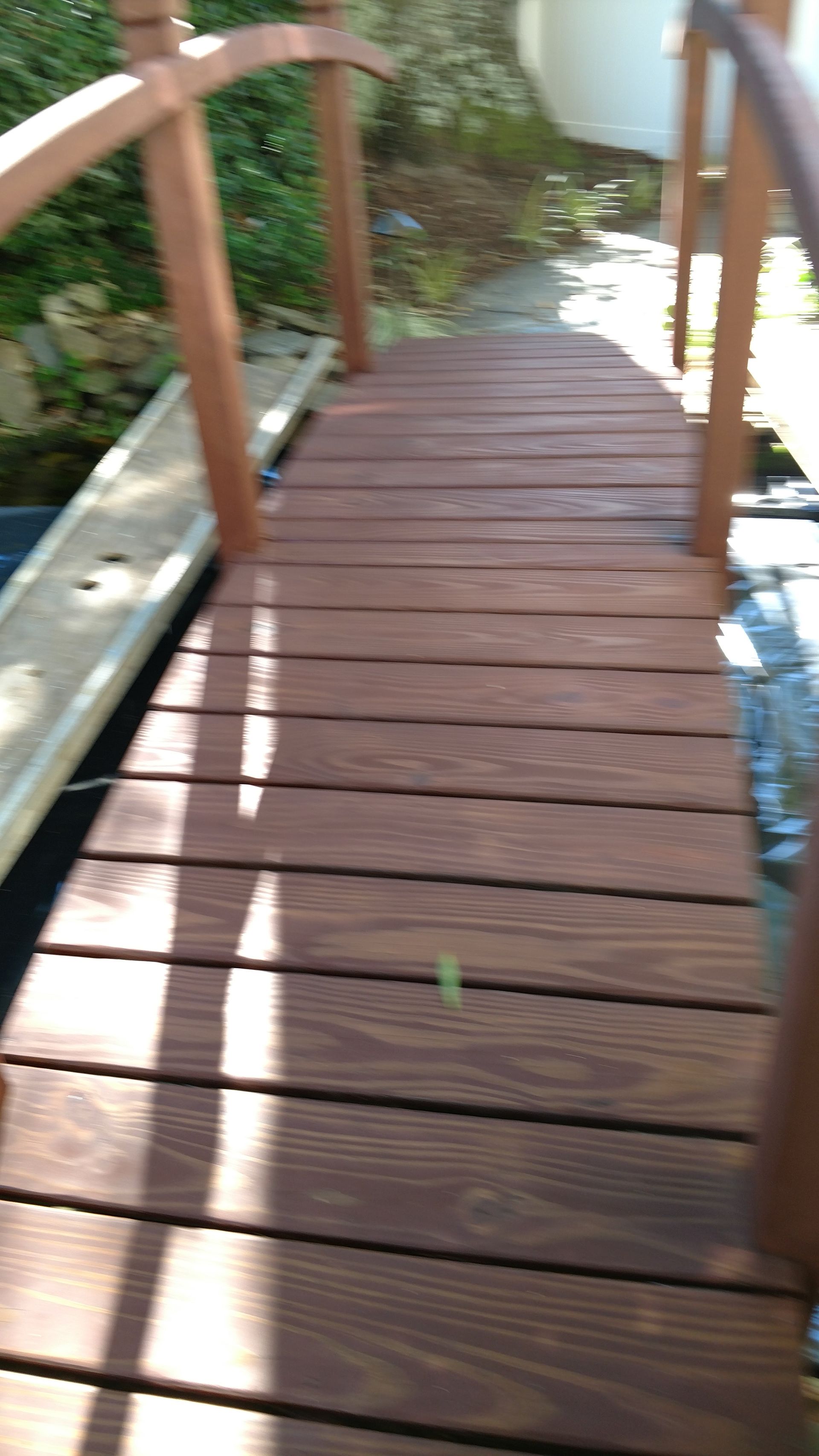 Wooden arched bridge over water. Brown wood, railings, sunny outdoor setting.