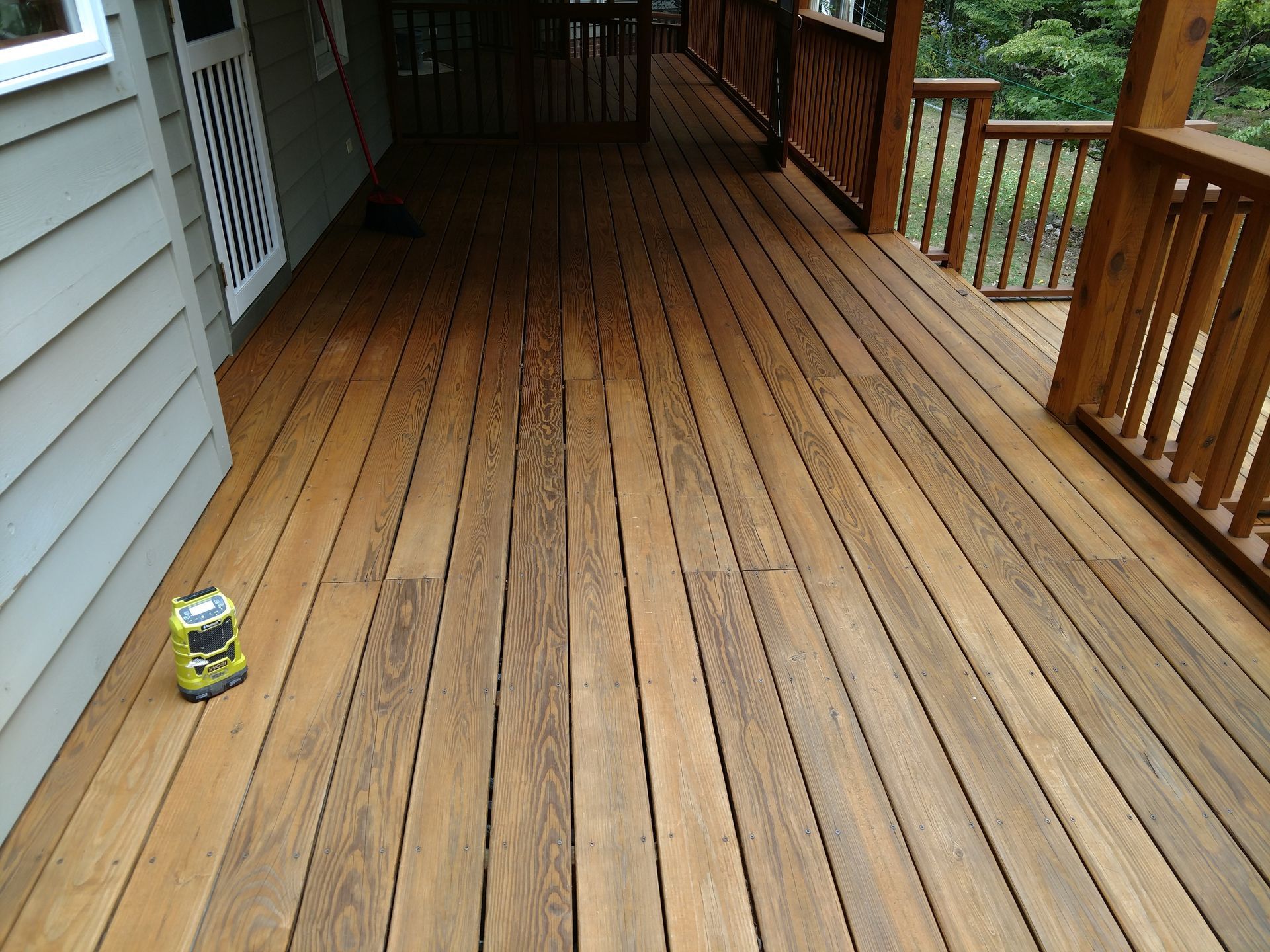 Wooden deck with dark stain, attached to a house with gray siding. A Ryobi tool sits on the deck.