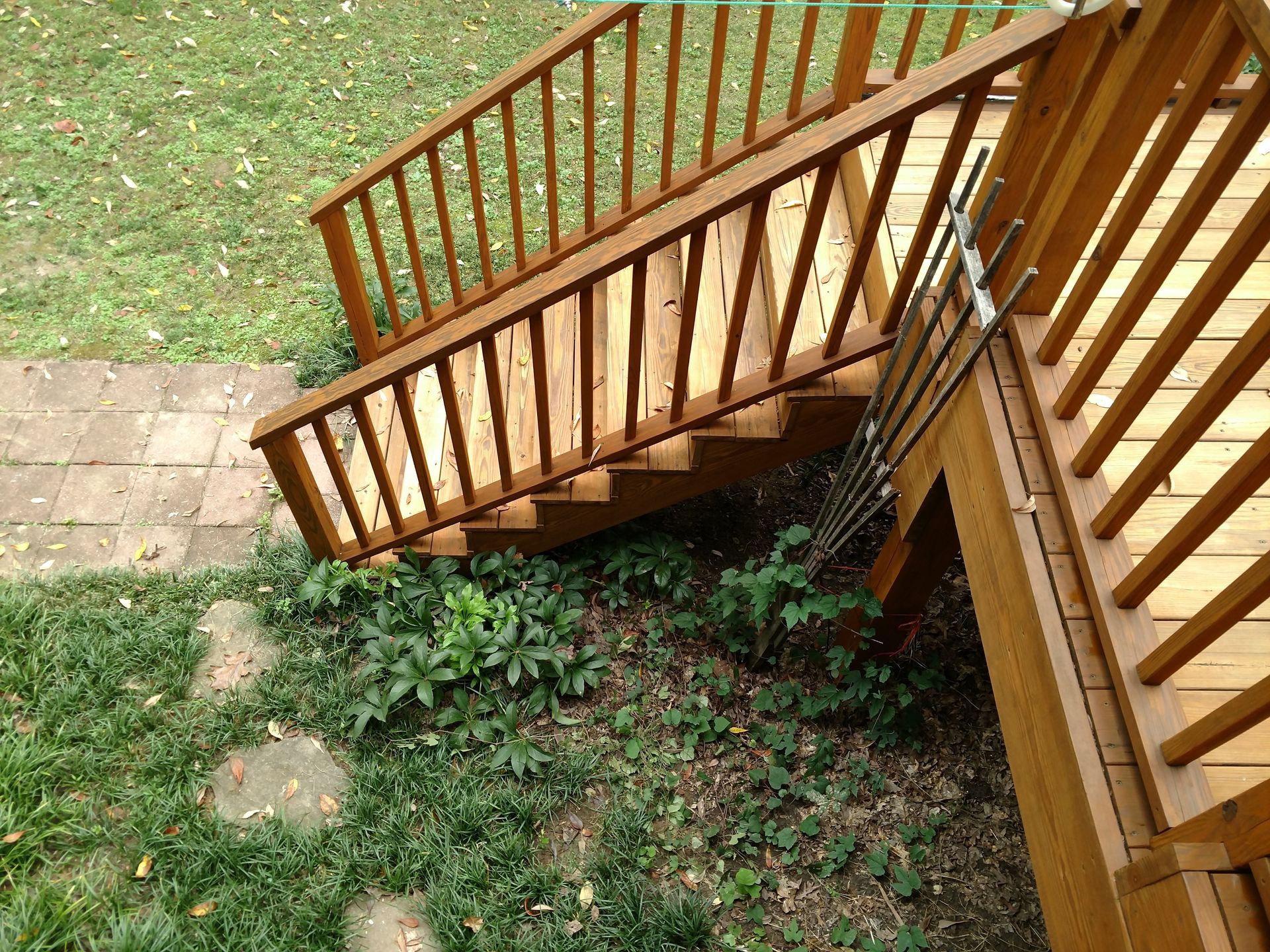 Wooden deck stairs leading down to a green yard with stone stepping stones and plants.
