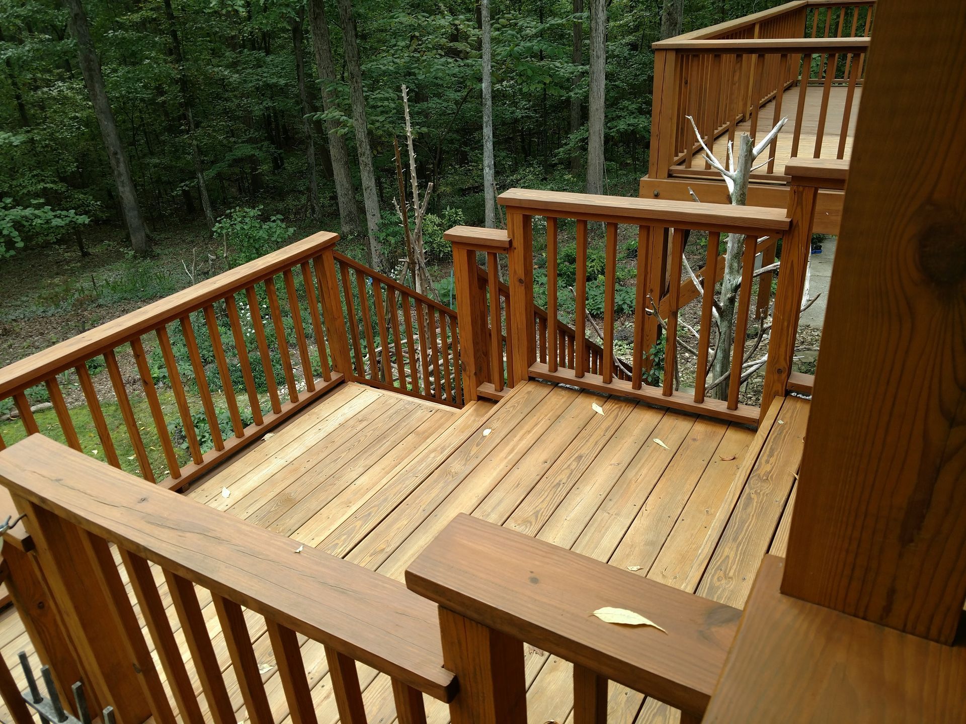 Wooden deck with stairs leading into a wooded area. Brown railing.