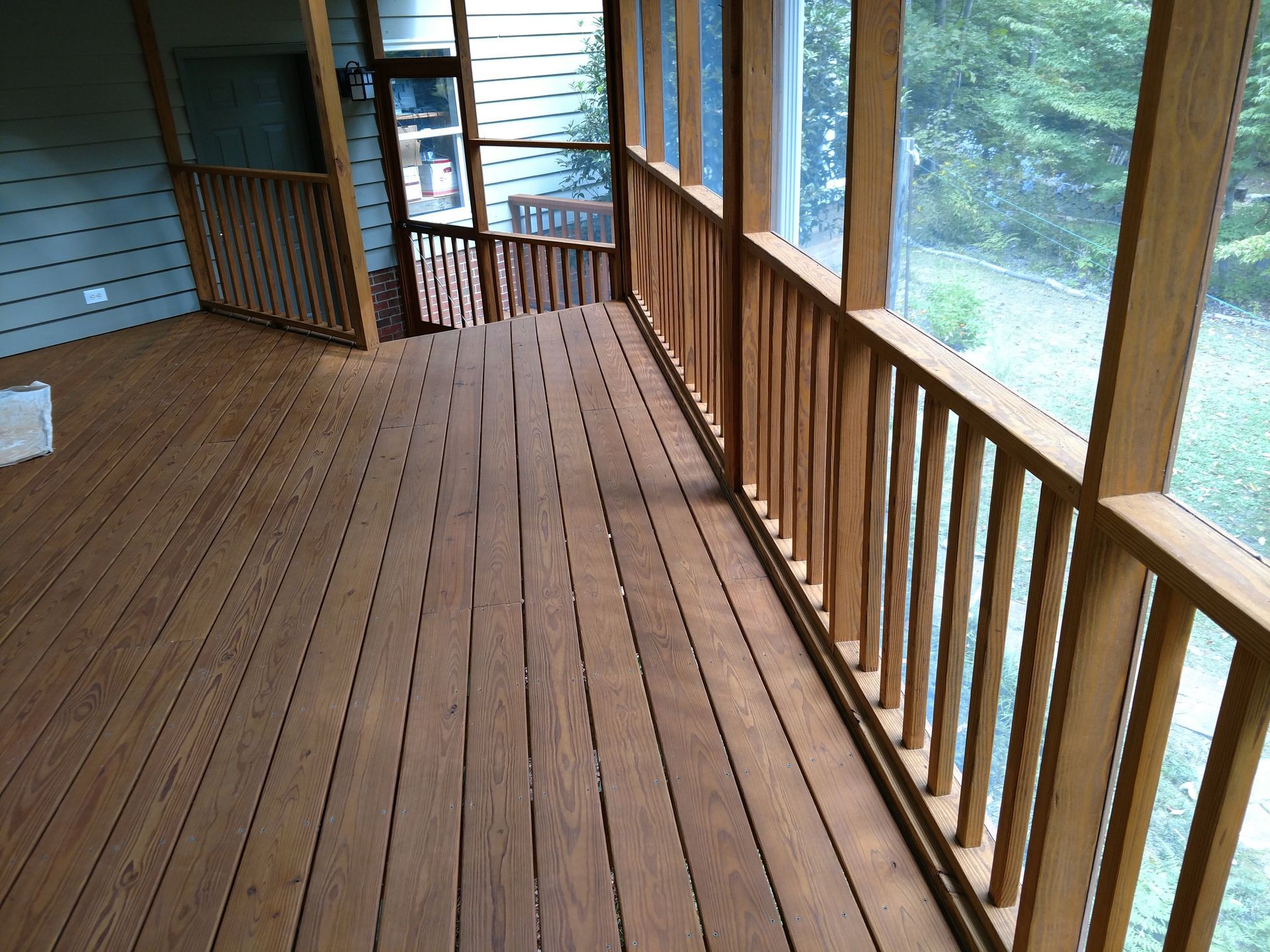 Wooden screened porch with railings, overlooking a grassy yard.