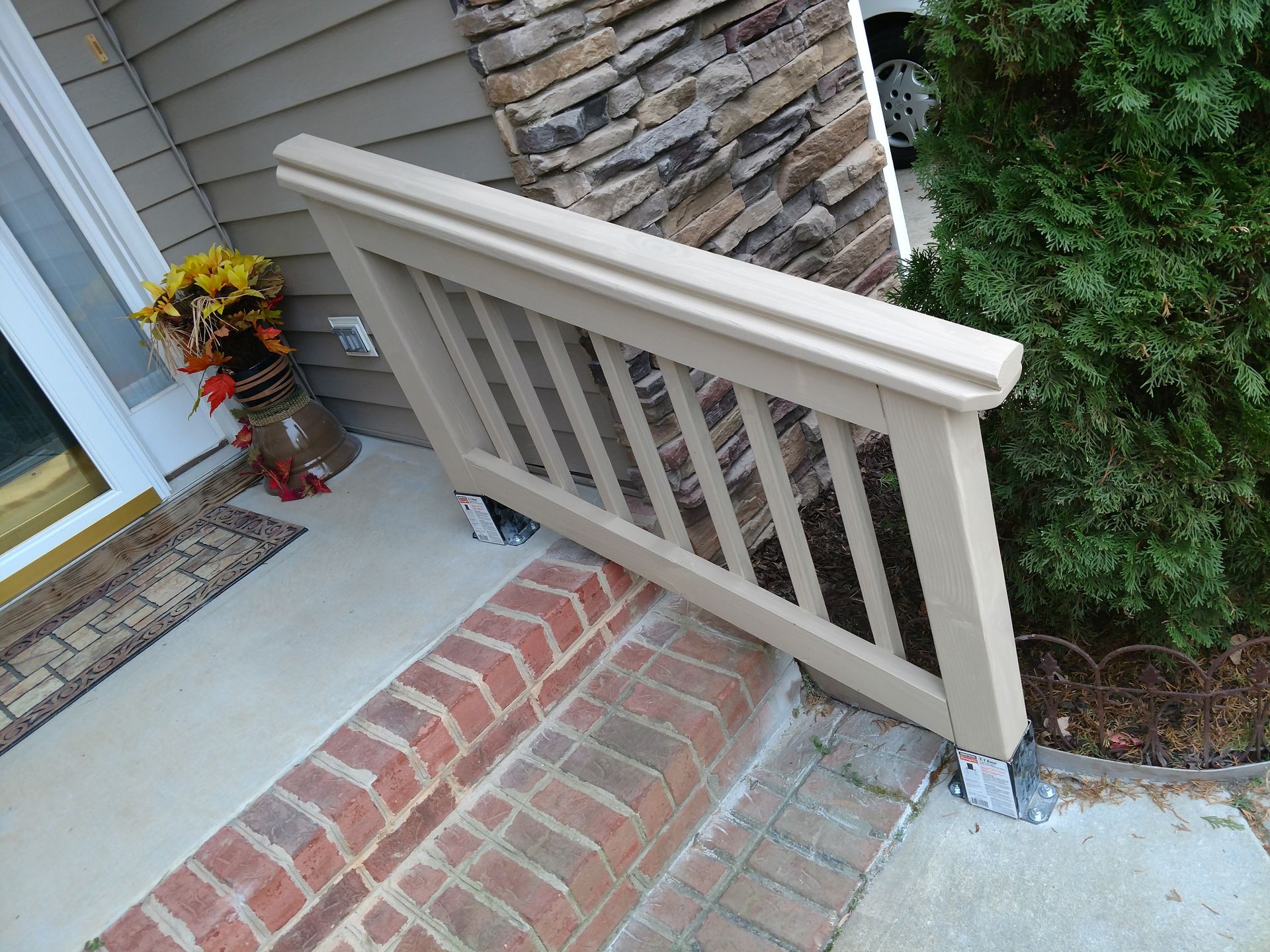 Beige railing angled over brick steps, leading to a front door with fall decor.