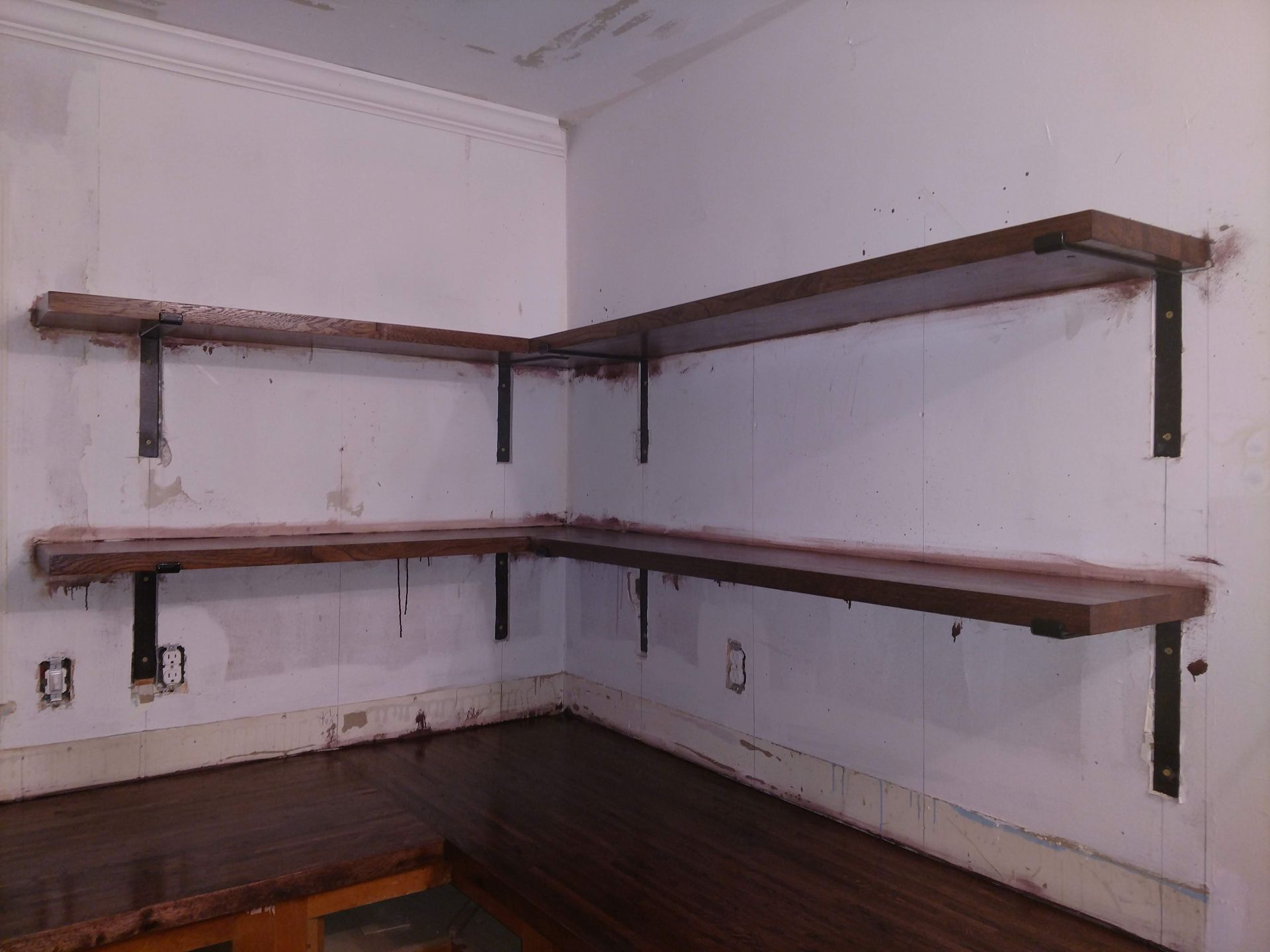 Brown wooden corner shelves mounted on black brackets in a white room.