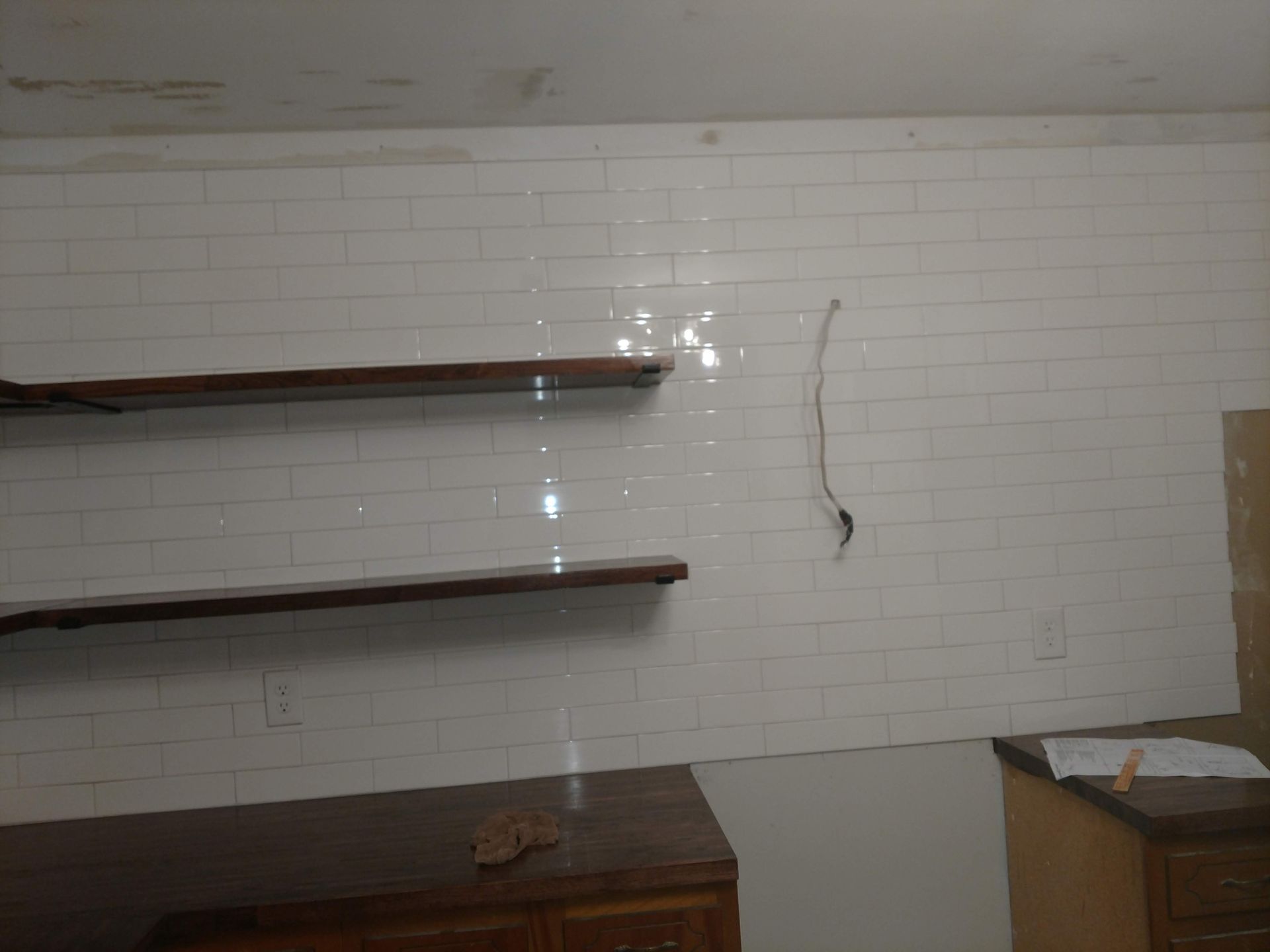 White tiled wall with wooden shelves. A dark cabinet sits below.