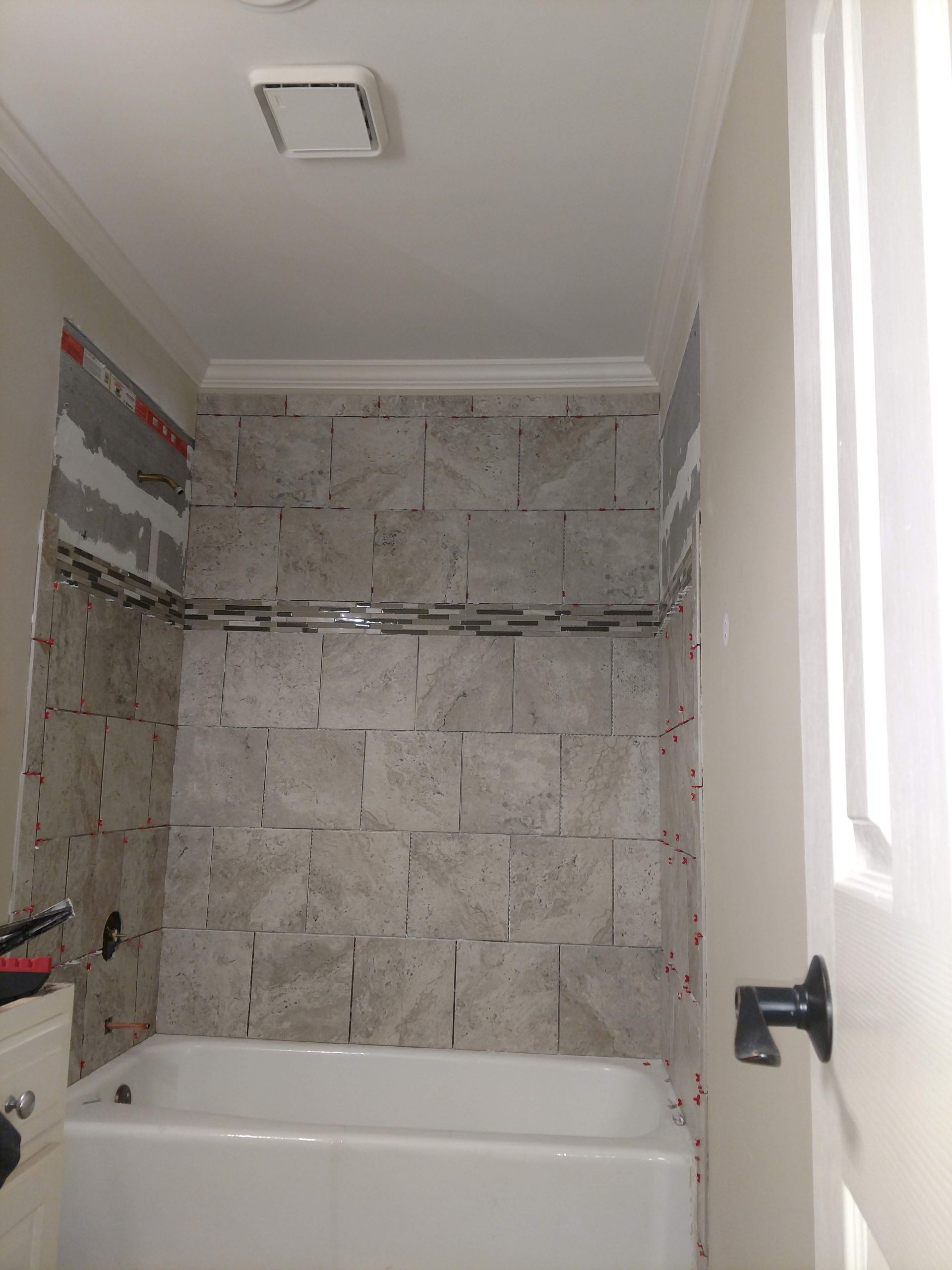 Bathroom with a tiled wall above a white bathtub, door on the right.
