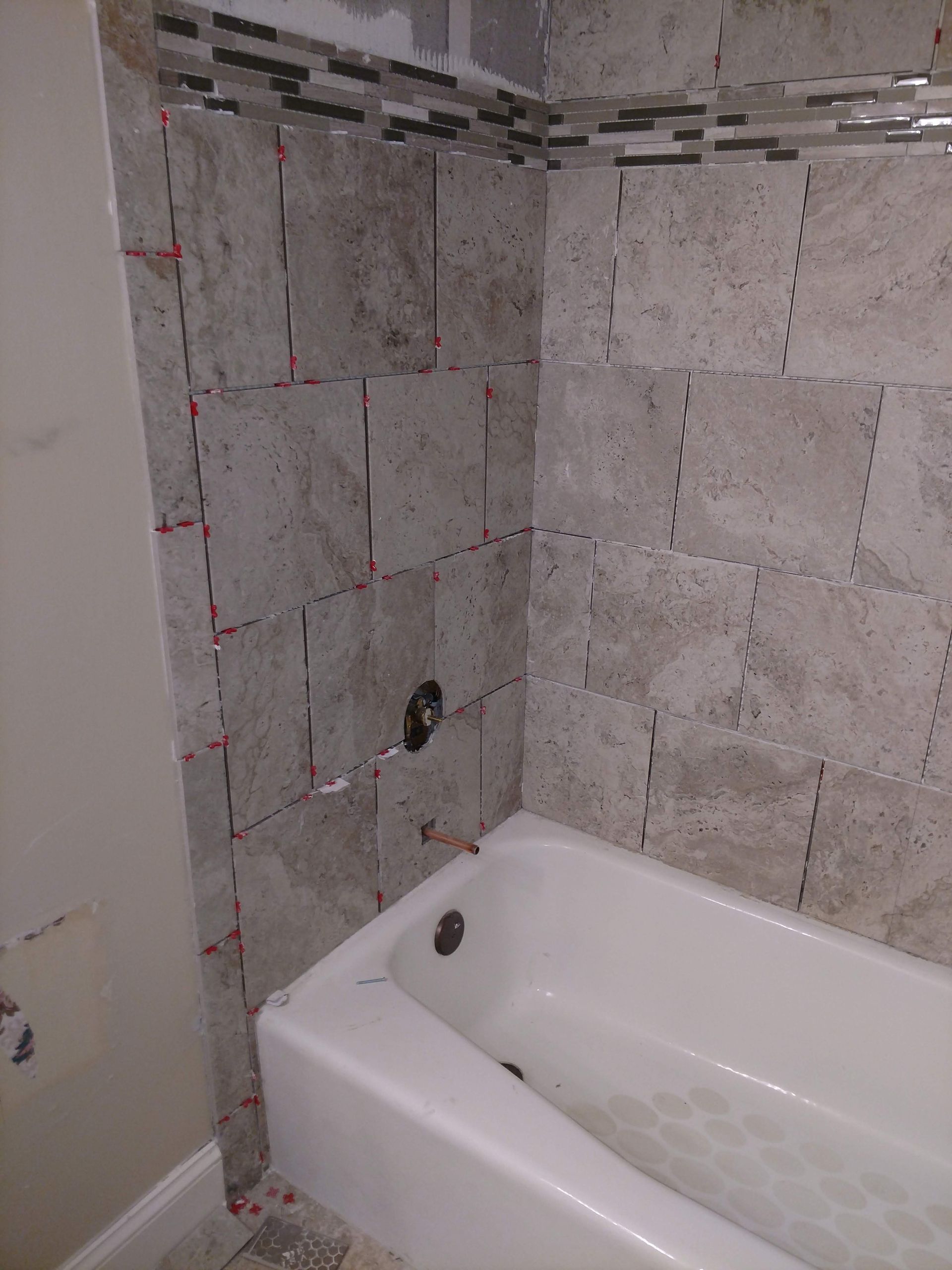 Bathroom with tiled walls in progress, bathtub in foreground, tile spacers visible.