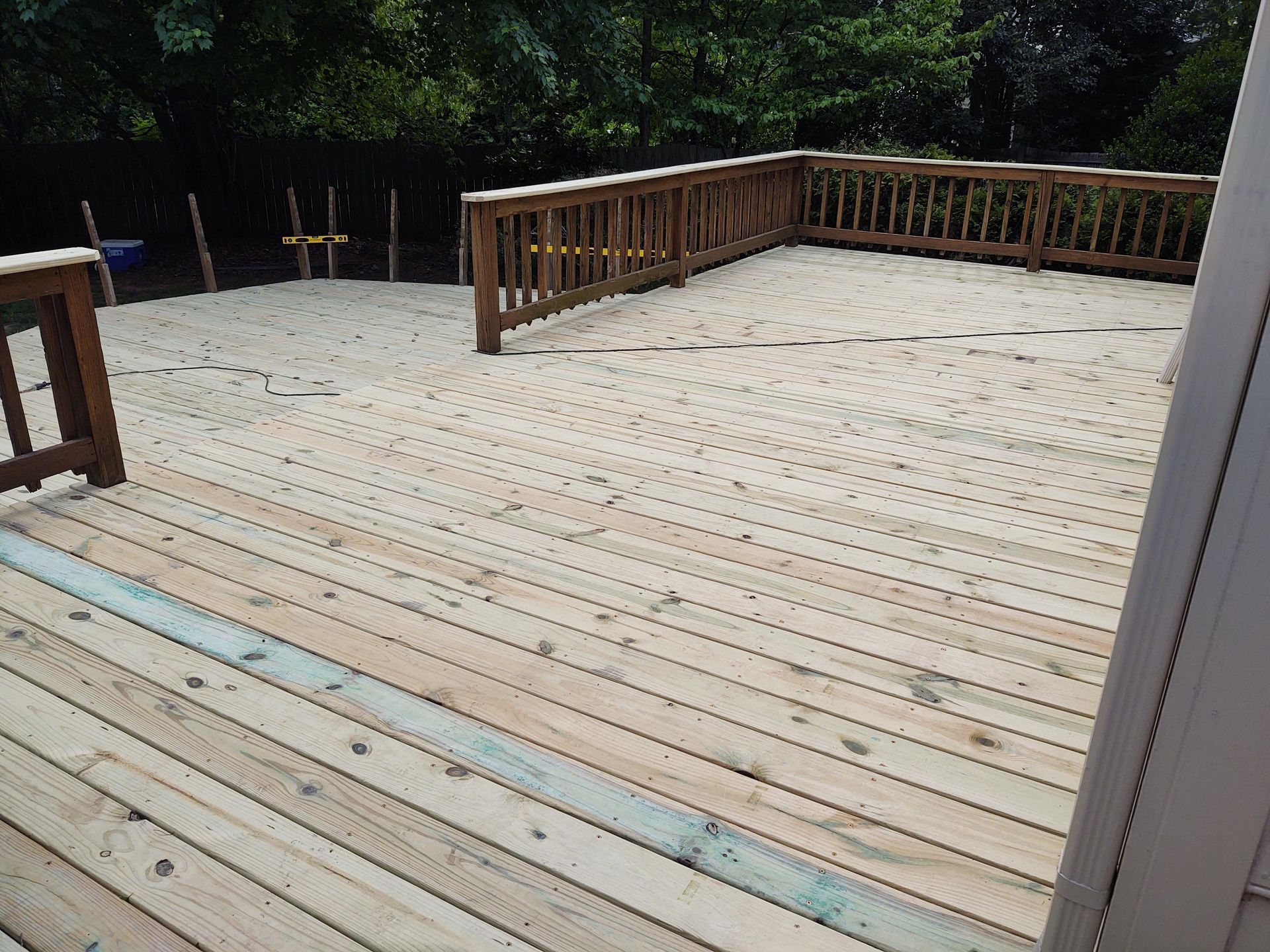 Wooden deck with railings, extending to a sand-covered area, trees in the background.