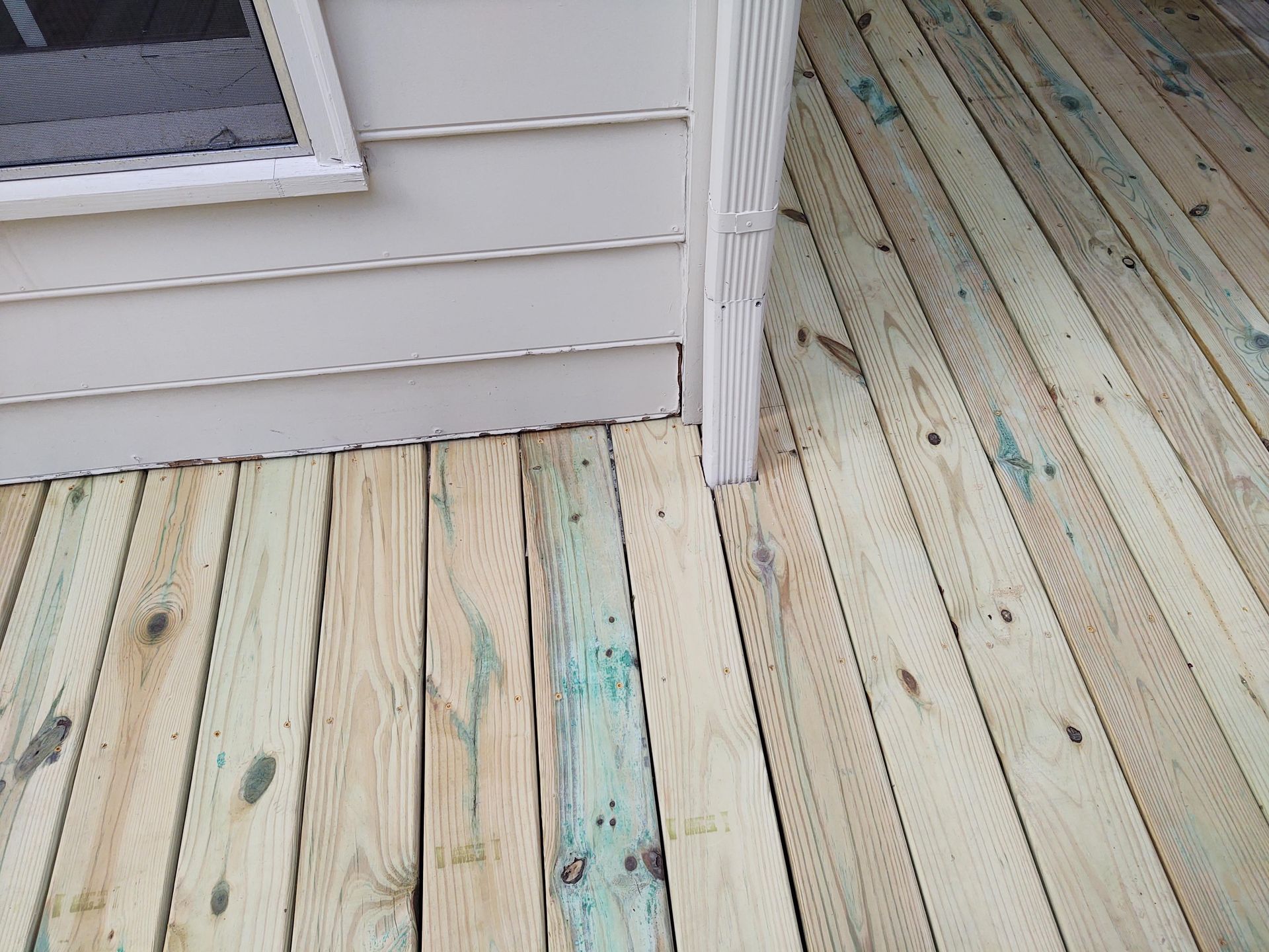 Wooden deck boards meet siding and downspout of a building.