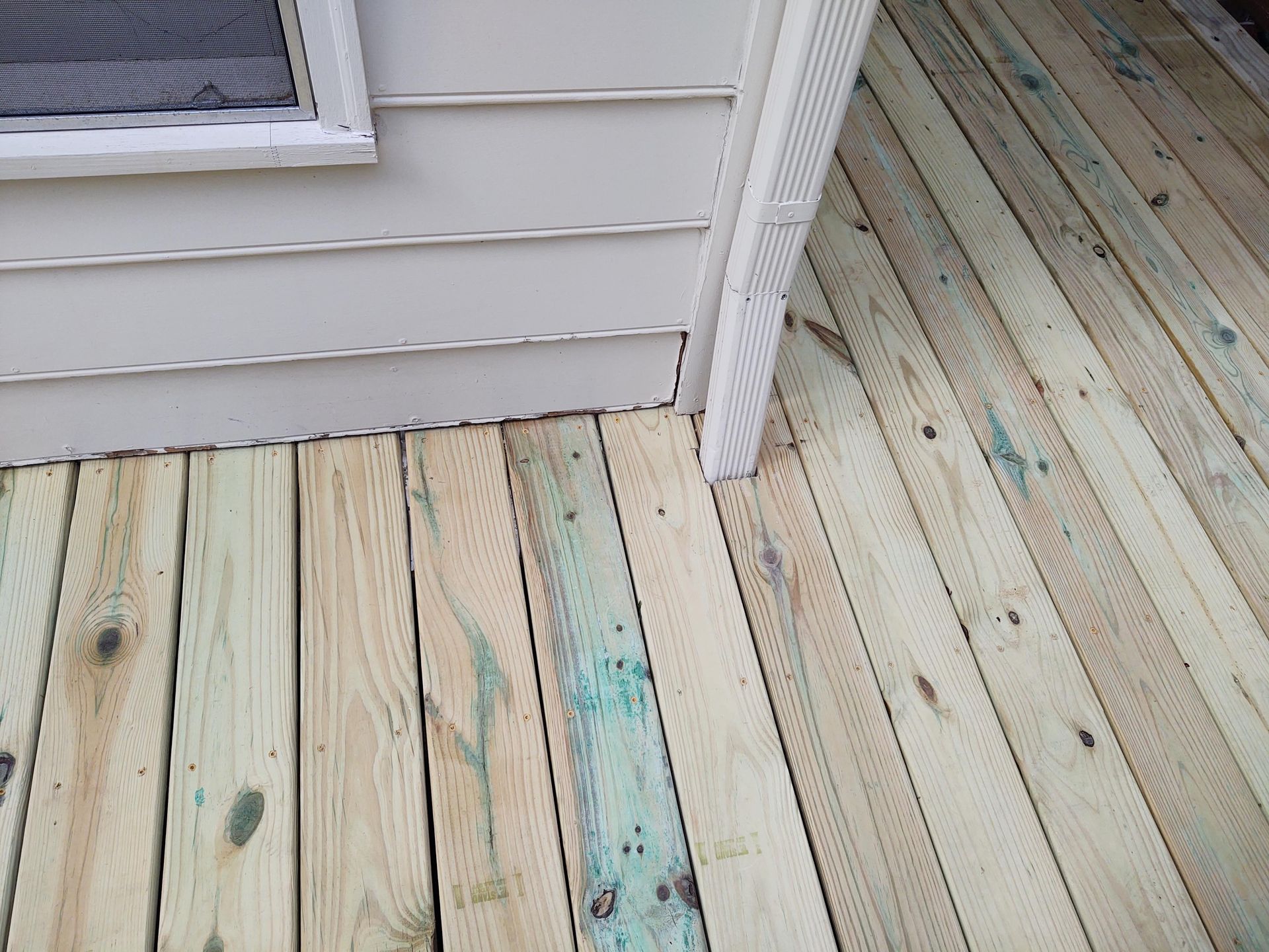Wooden deck attached to a building's white siding and corner trim. Boards show traces of blue stain.