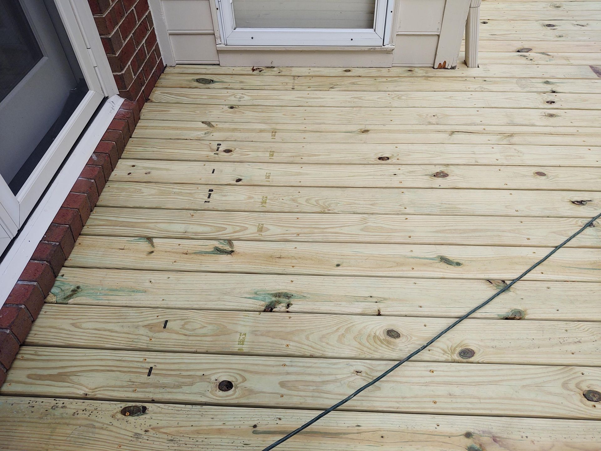 Wooden deck next to a brick wall and a window, with several screws visible.