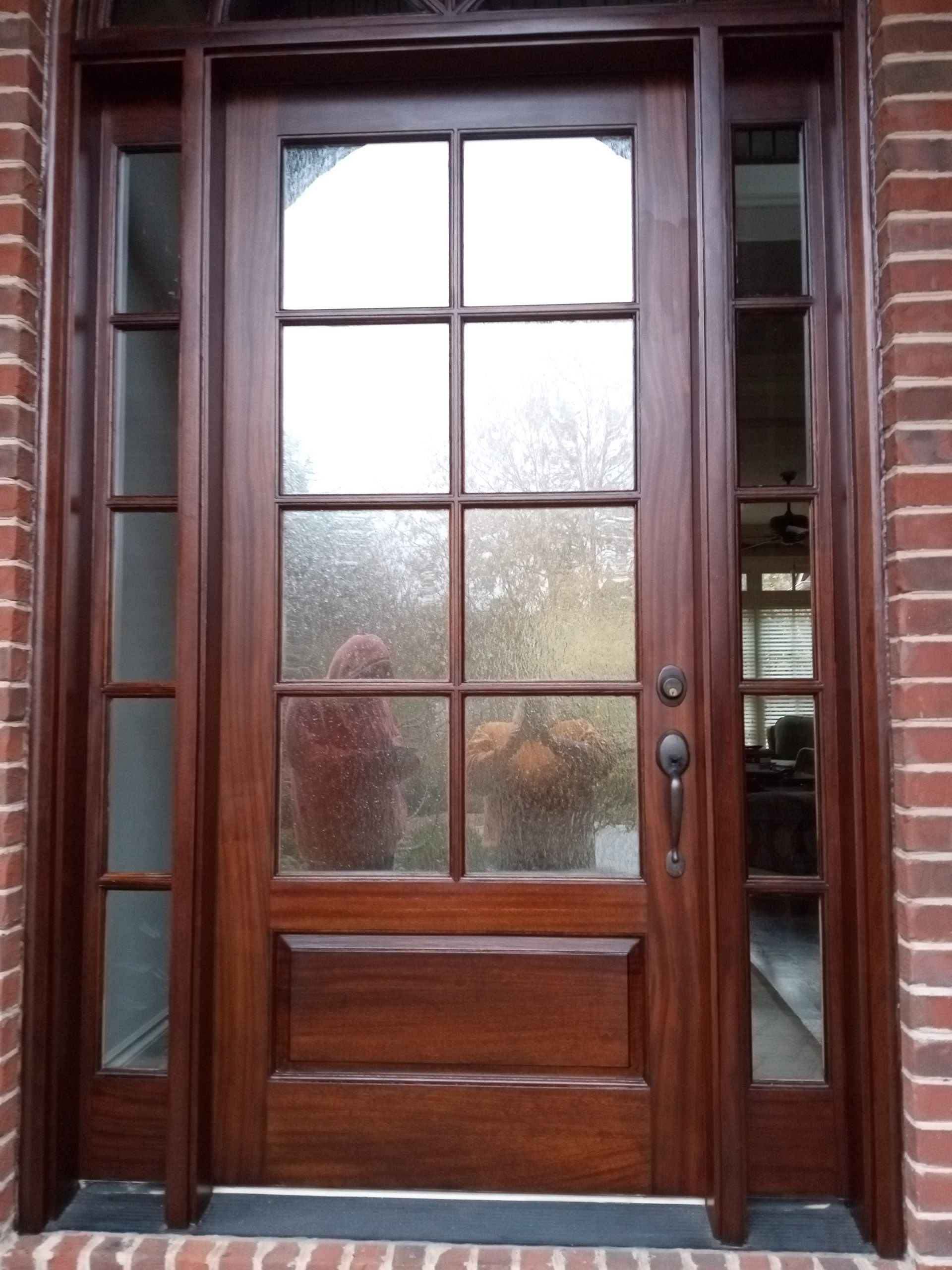 Brown wooden front door with glass panels, sidelights, and brick surround.