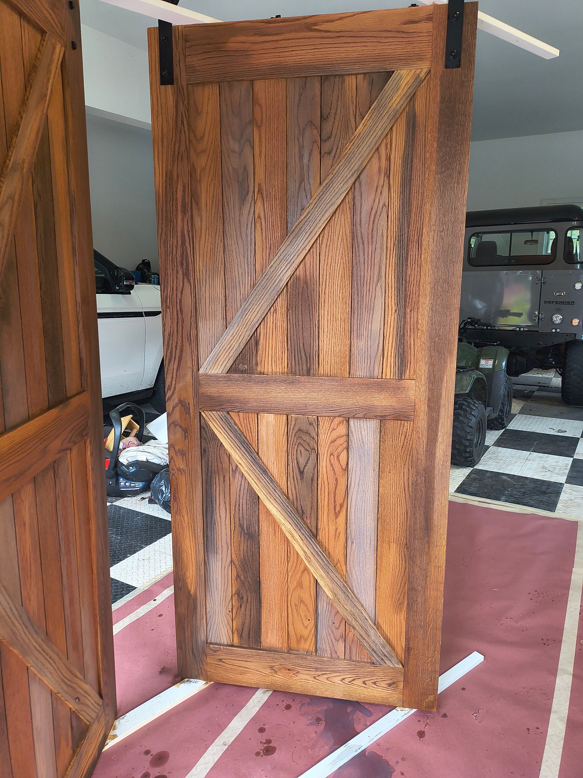 Barn-style wooden door with a diagonal brace, hanging on a black metal track, sitting on a checkered floor.