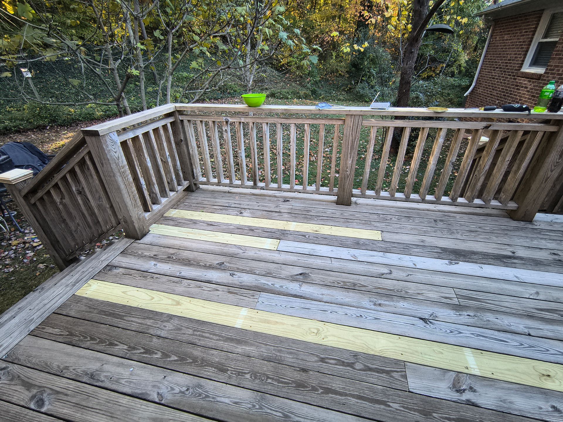 Wooden deck with railing, weathered boards, and a green bowl on the railing.