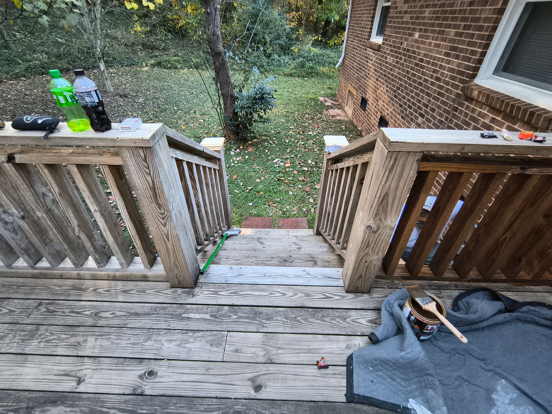 Wooden deck stairs leading to a backyard. Two soda bottles, a remote, and a blanket are on the deck.