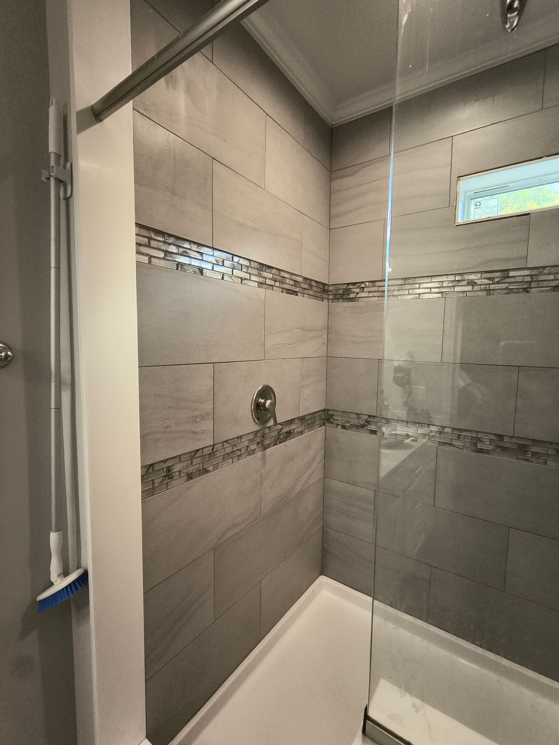 Gray tiled shower with glass door and decorative tile border.