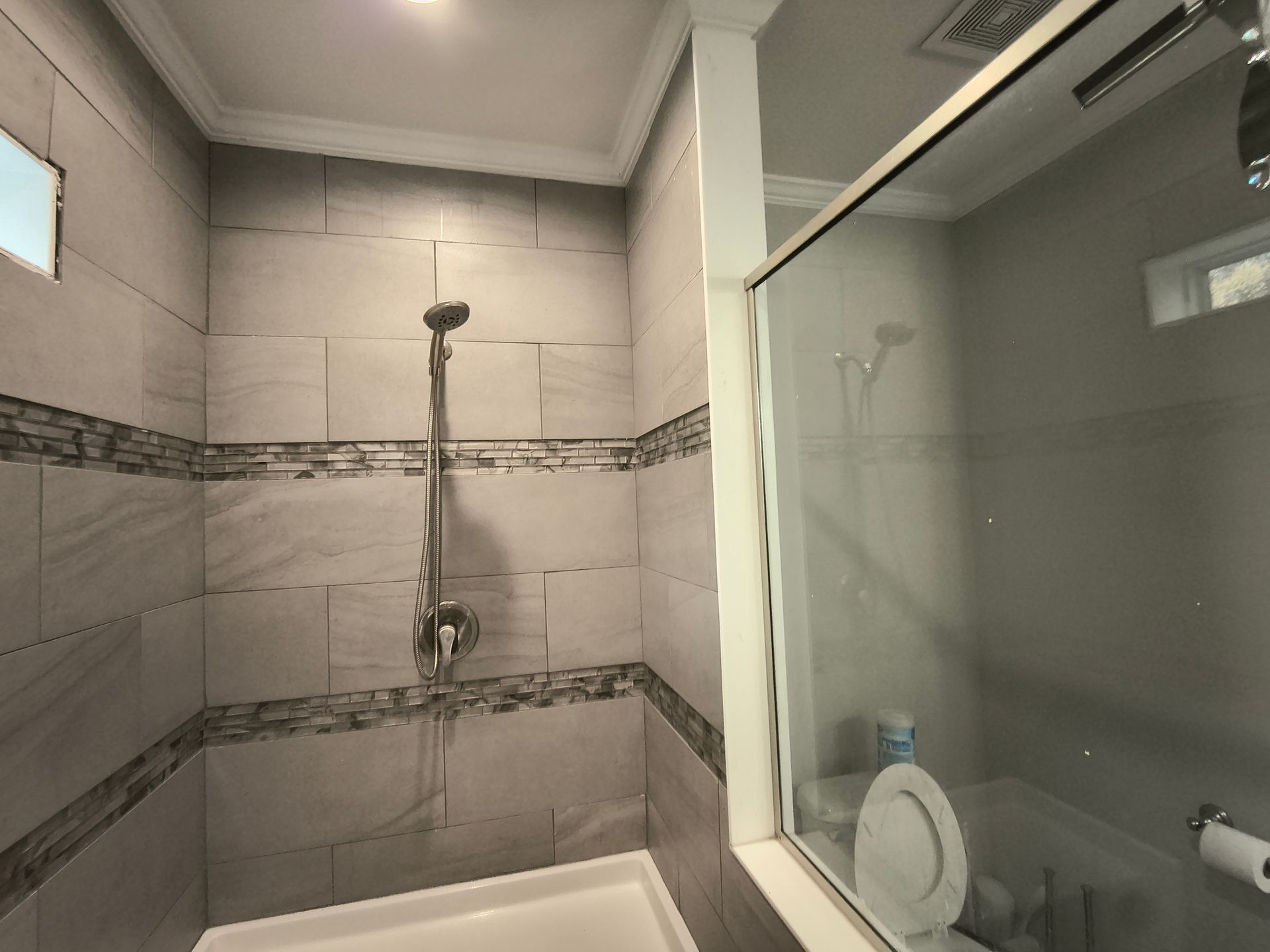 Bathroom shower with gray tiled walls, showerhead, and a glass door.