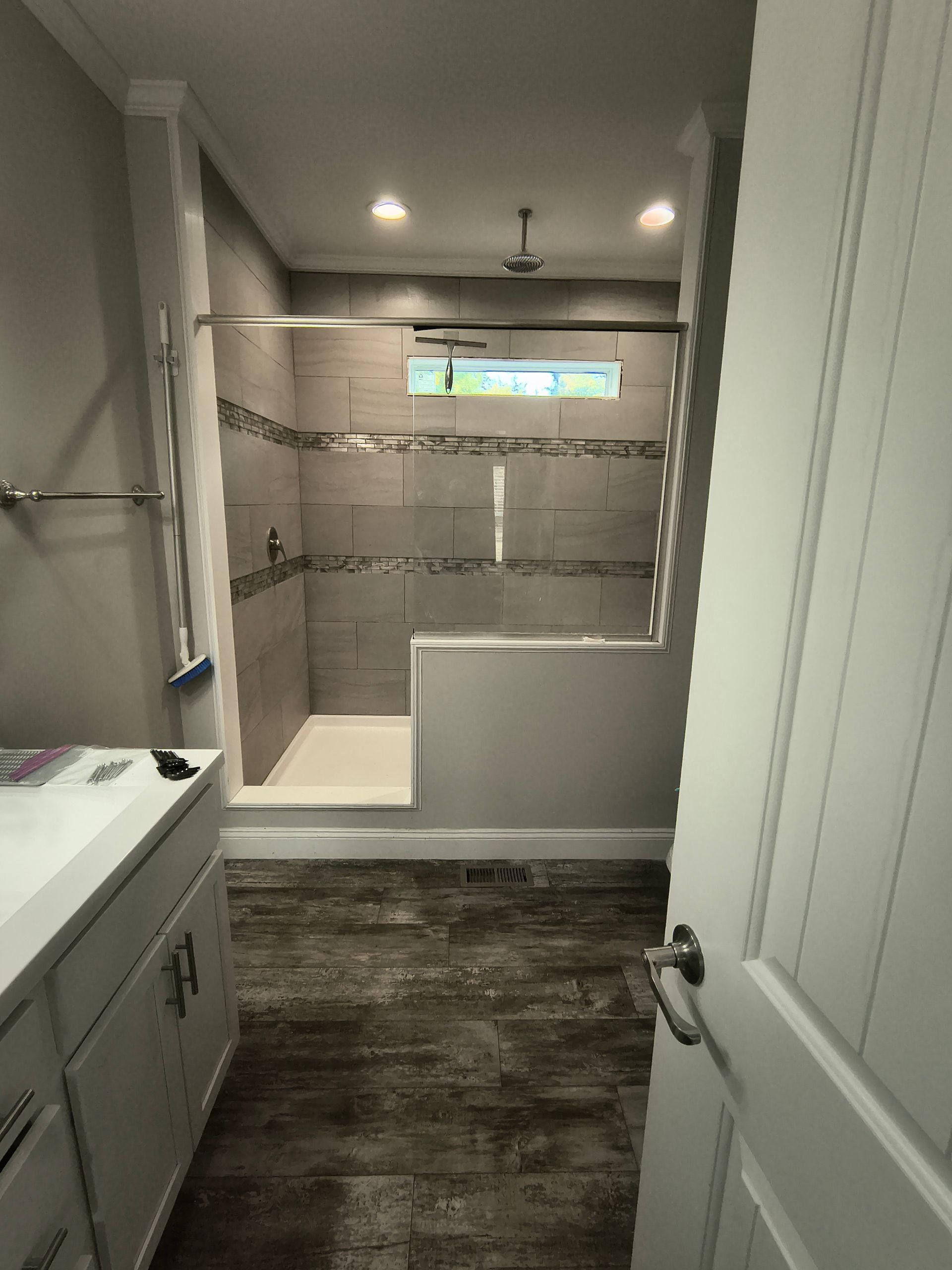 Bathroom with tiled shower, vanity, and wood-look flooring. Neutral colors, modern design.