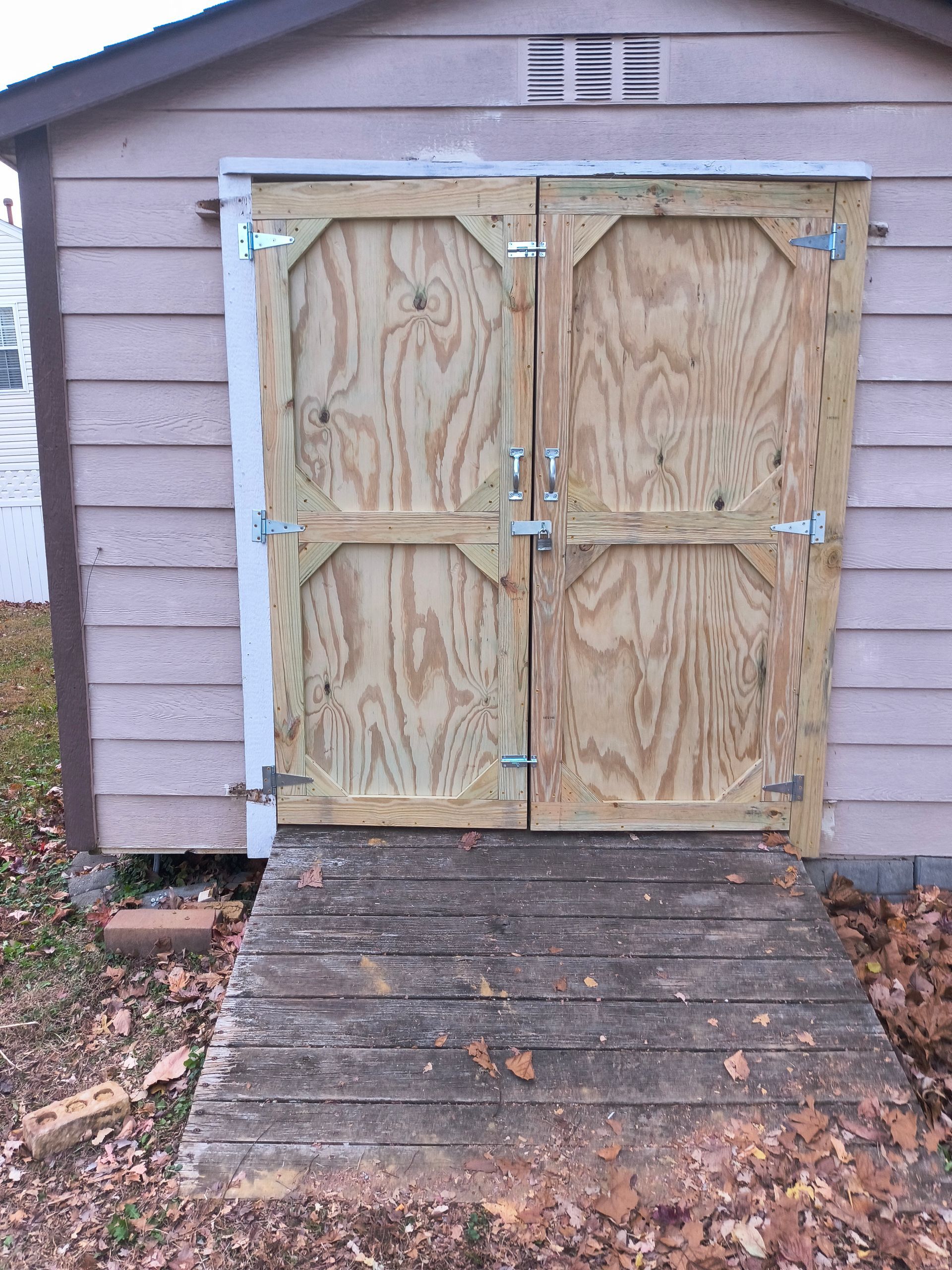 Wooden shed doors with ramp. Doors are unpainted plywood and secured by latches.