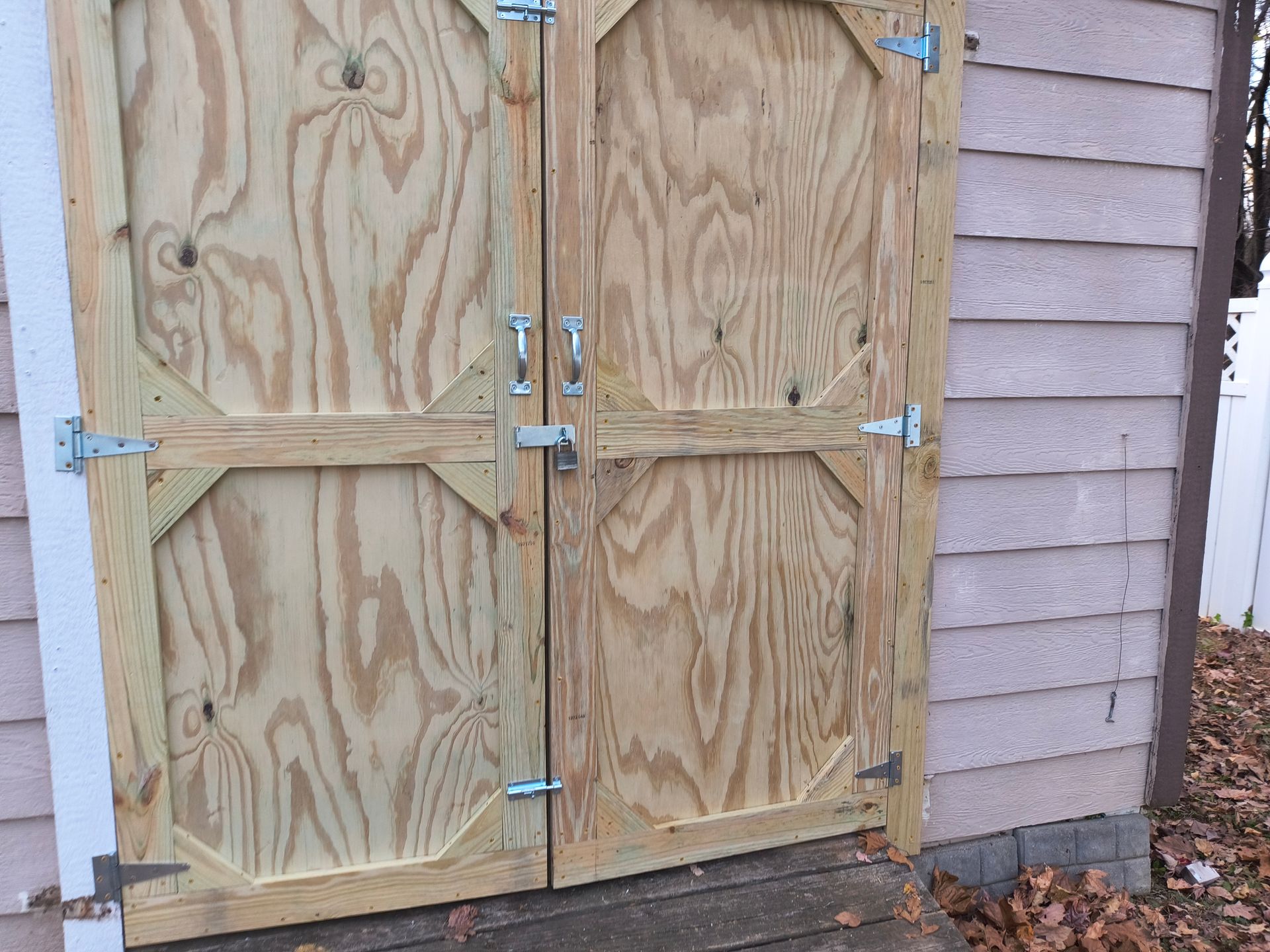 Wooden double doors with metal hardware, attached to a light pink building with brown trim.