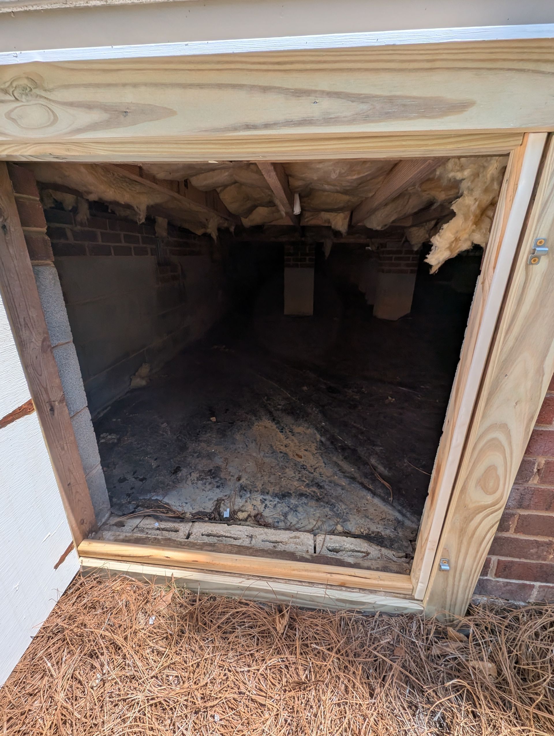 Open crawlspace entrance with exposed insulation and debris.
