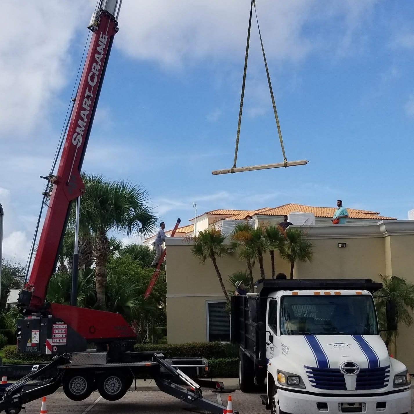 Crane lifting roofing materials onto a house beside a white truck under a blue sky