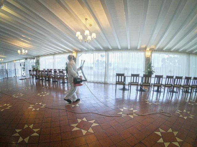 Persona con tuta protettiva che spruzza una grande stanza con sedie e tende.