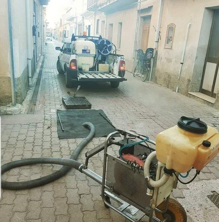 Un camion con delle attrezzature è parcheggiato su una strada lastricata; un tubo flessibile arriva fino a un accesso fognario aperto.