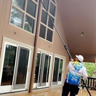 A man efficiently using a power washer to clean the windows and front of a house, removing dirt and grime with a high-pressure stream of water.