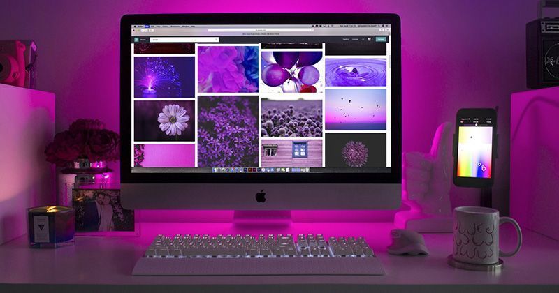 a computer monitor is sitting on a desk with purple lights behind it.