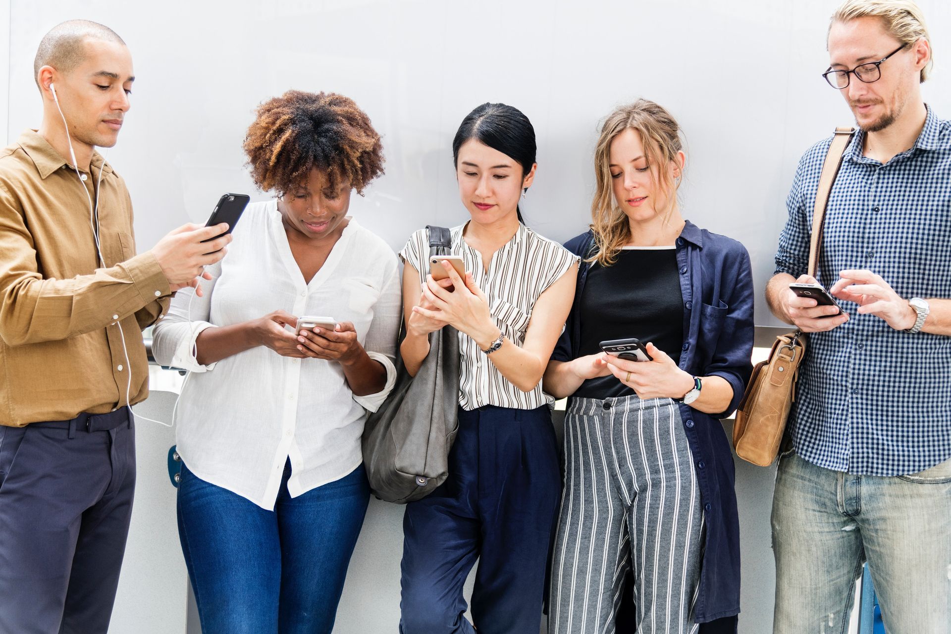 A group of people are standing next to each other looking at their phones.