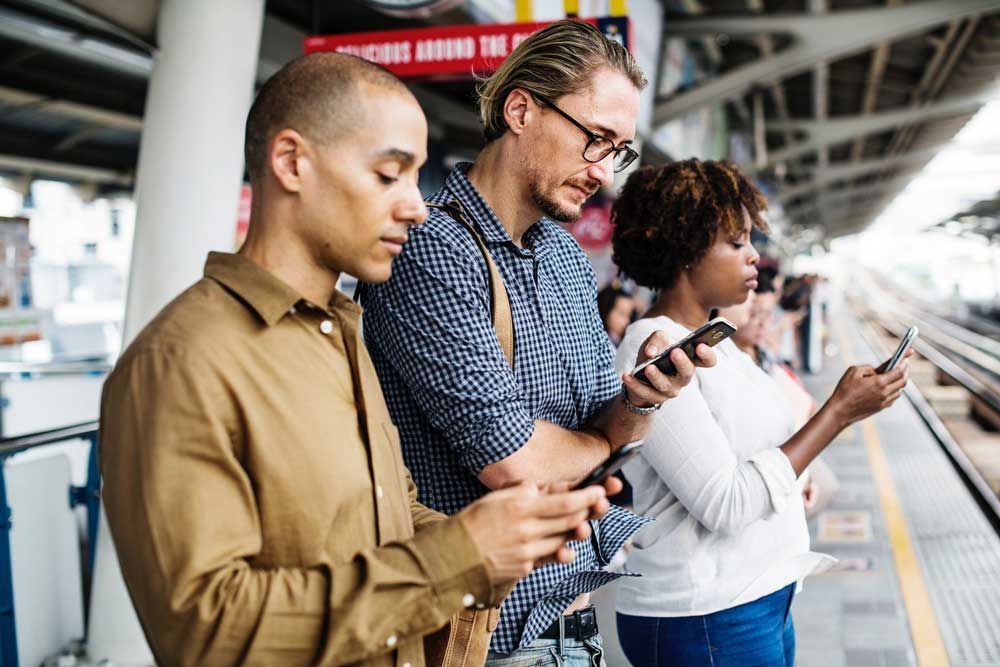 A group of people are looking at their phones at a train station.