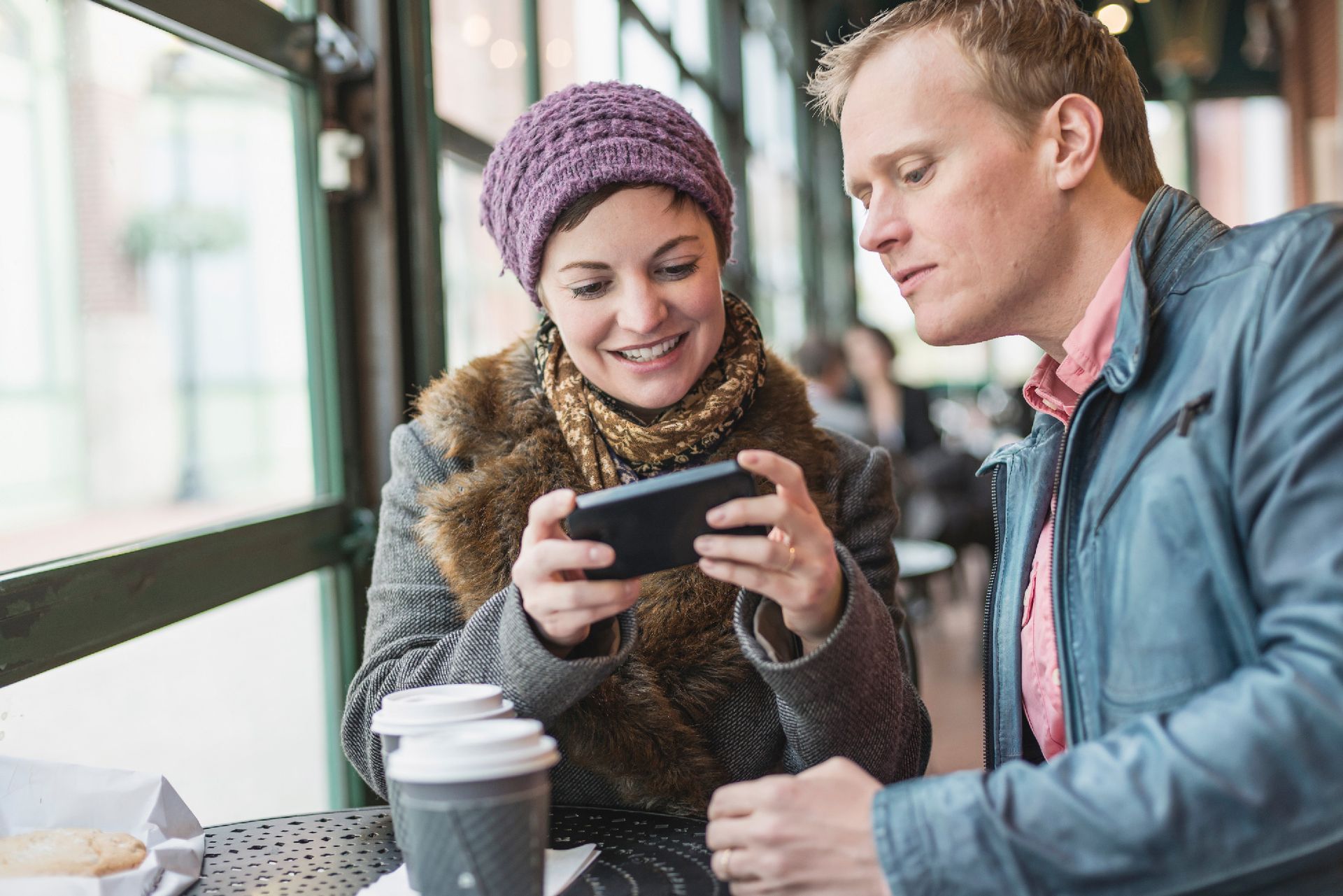 A man and a woman are sitting at a table looking at a cell phone.