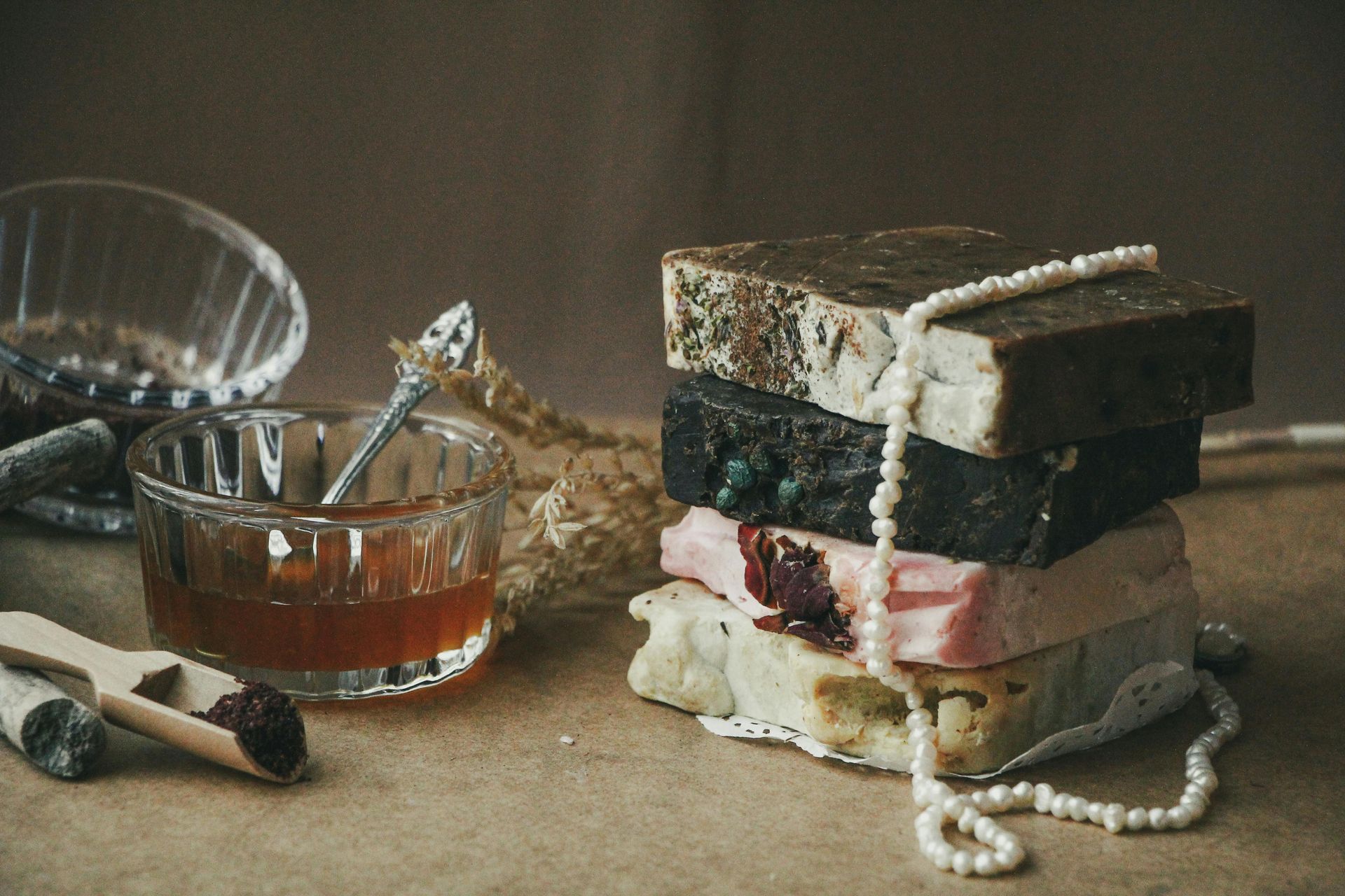 Stack of colorful soaps with a pearl necklace, jam in a glass bowl, and a small wooden scoop.
