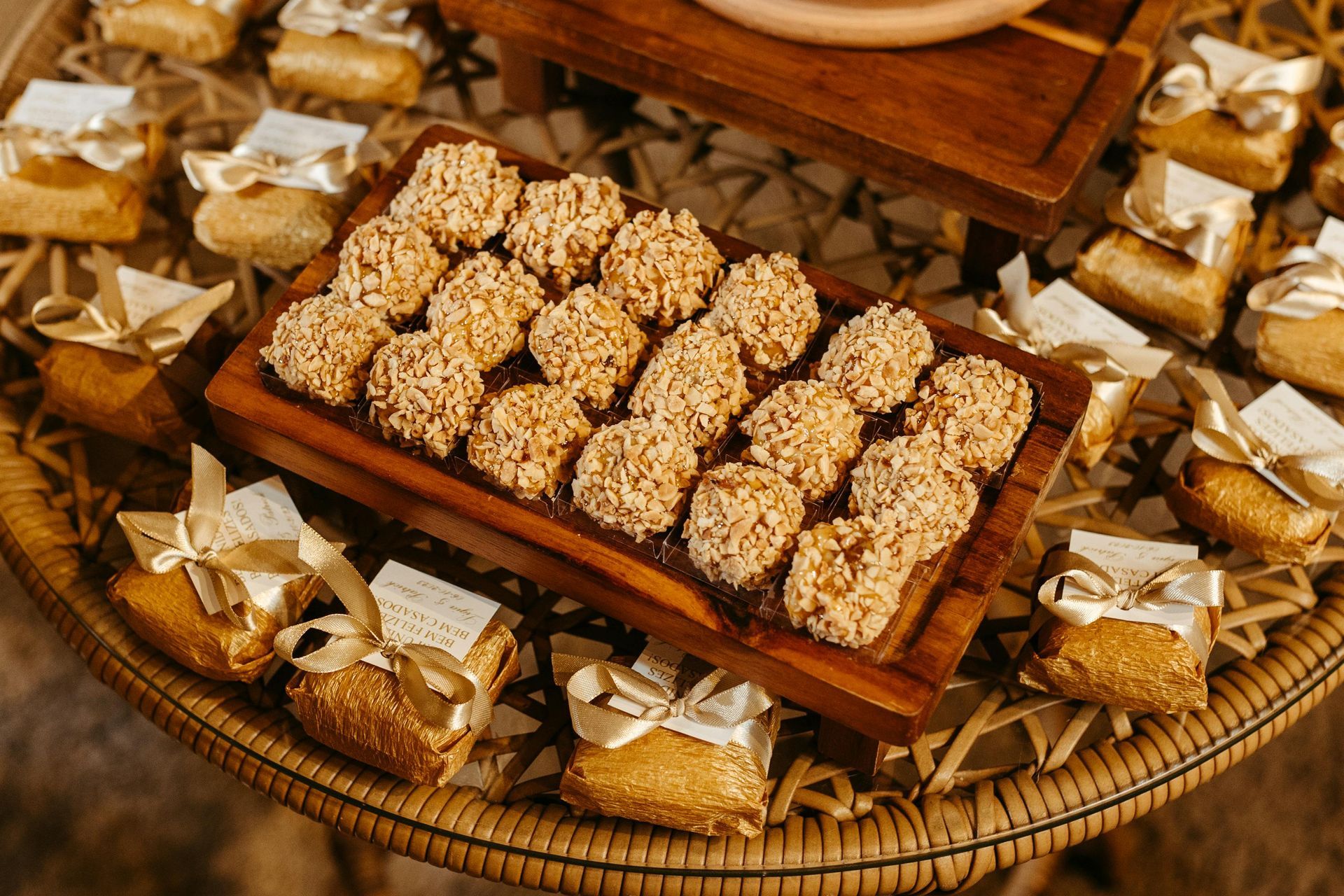 Rice crispy treats on a wooden tray, surrounded by small wrapped gifts with ribbons, on a woven table.