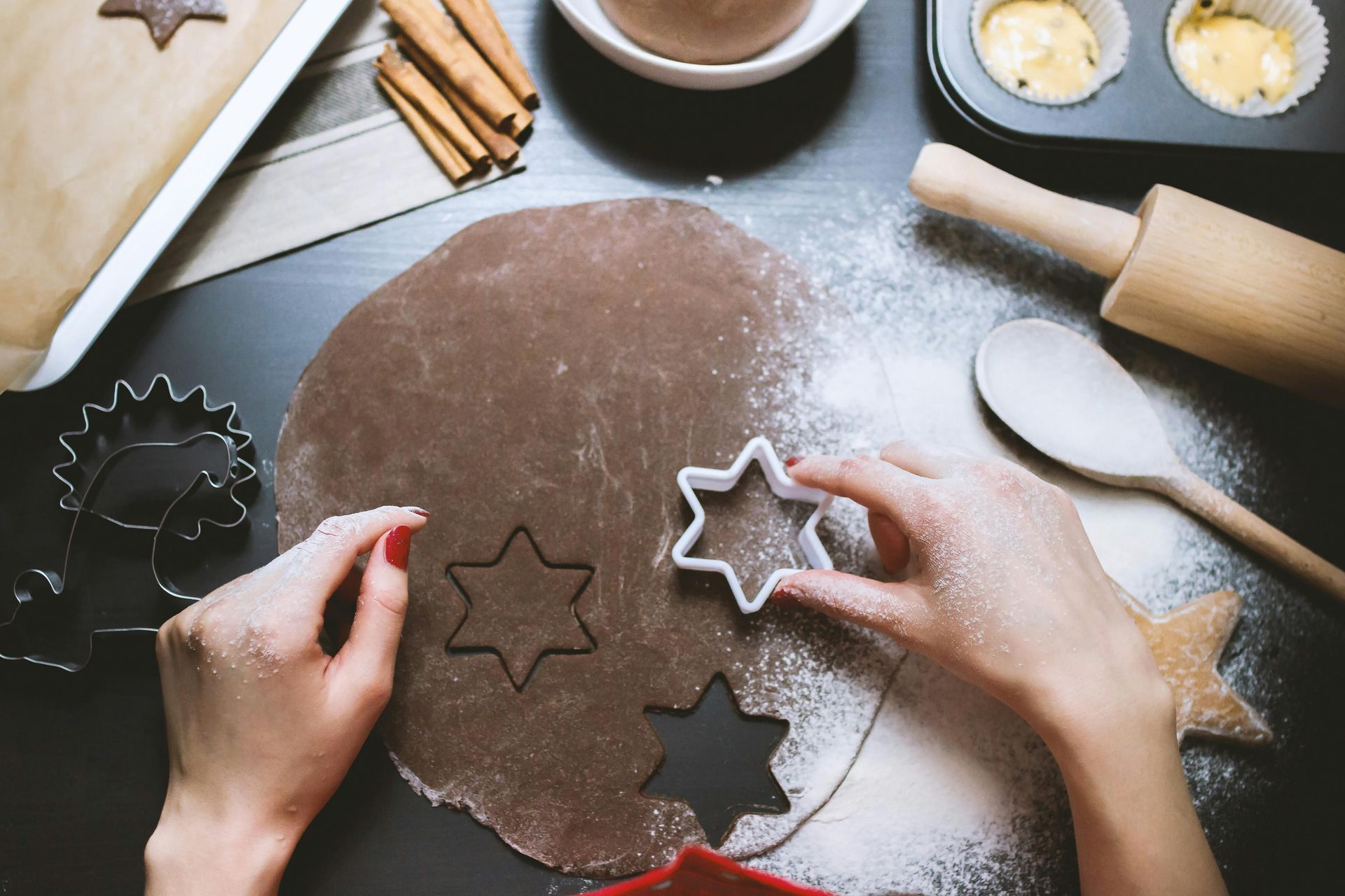 Hands cutting star shapes from rolled dough; baking supplies on table.