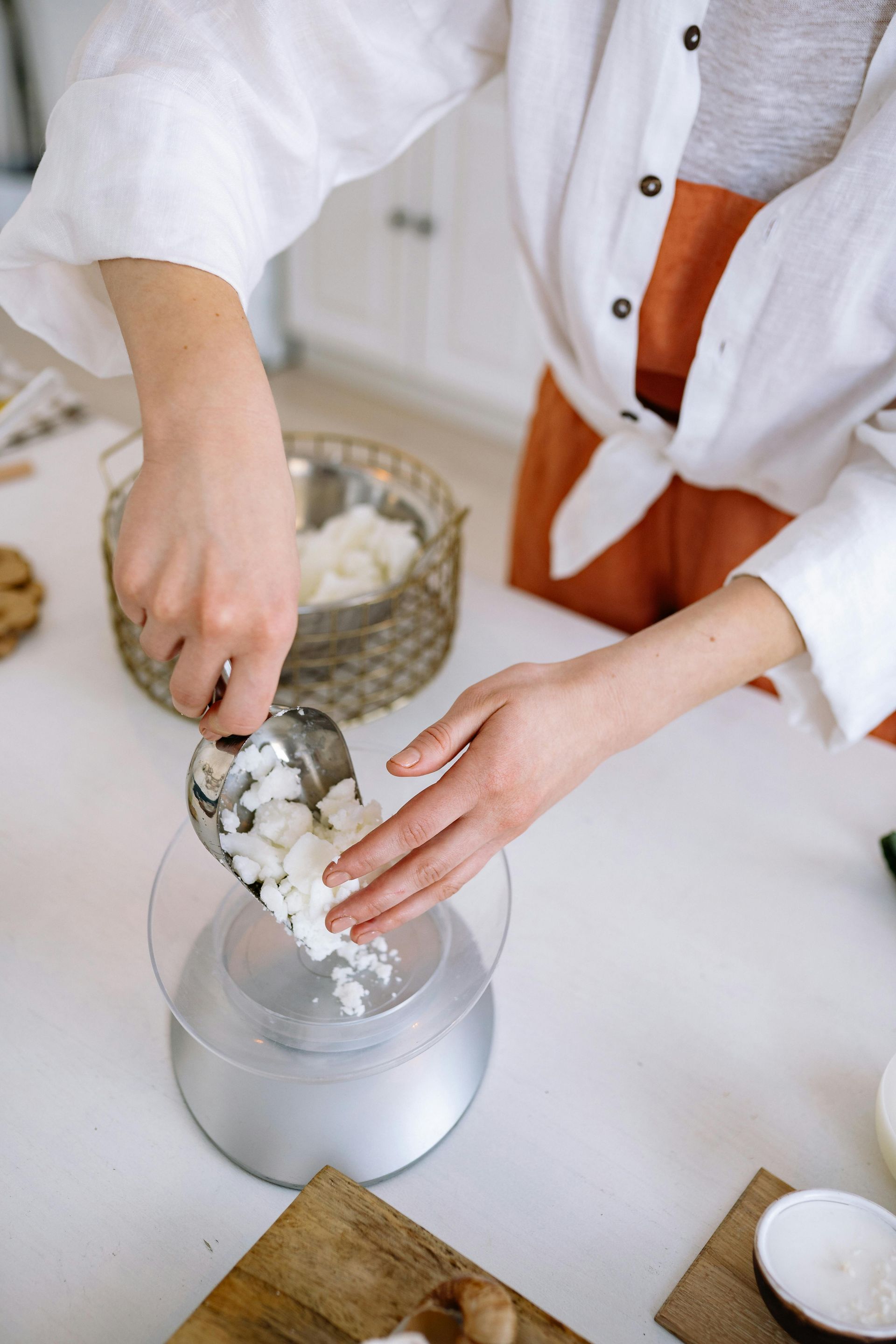 Person measuring wax chunks with a scoop onto a scale, preparing for candle making.